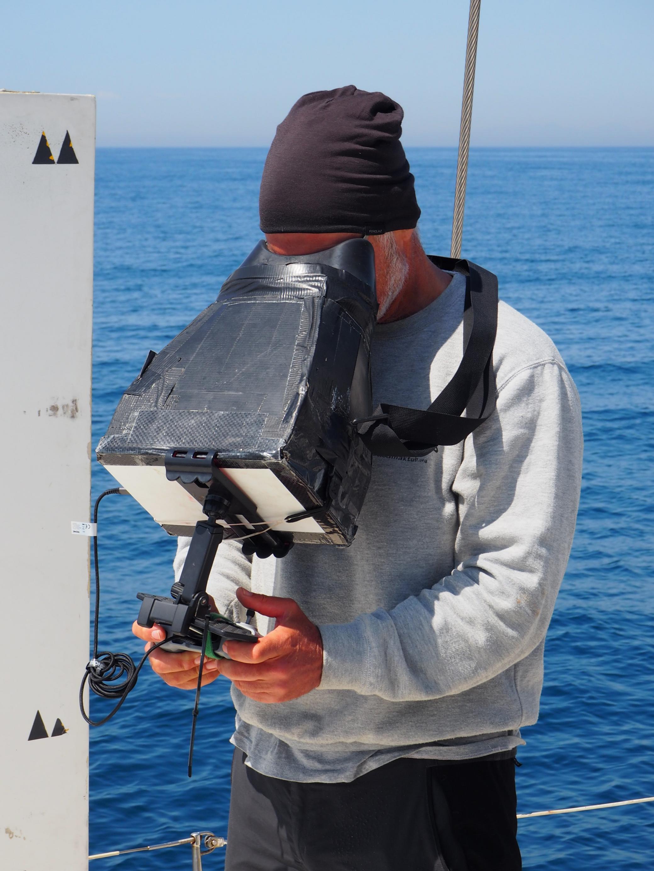 Mann mit schwarzer Mütze und einem grauen Sweatshirt mit Aufdruck: Edmaktub.org „Projekte Rorqual“ steuert eine Drohne