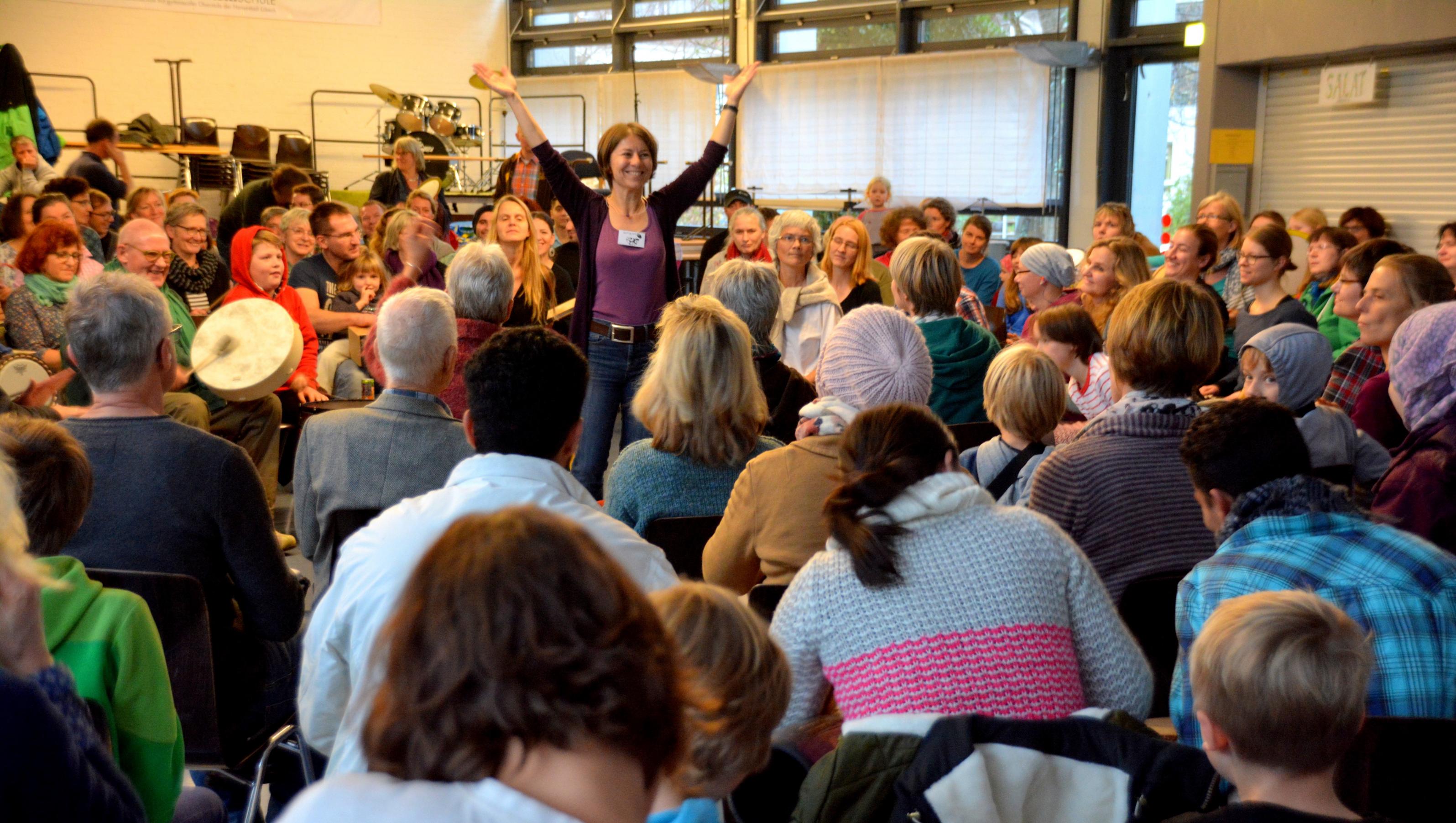 Helga Reihl steht in der Mitte eines Stuhlkreises und leitet das gemeinsame Trommeln an.