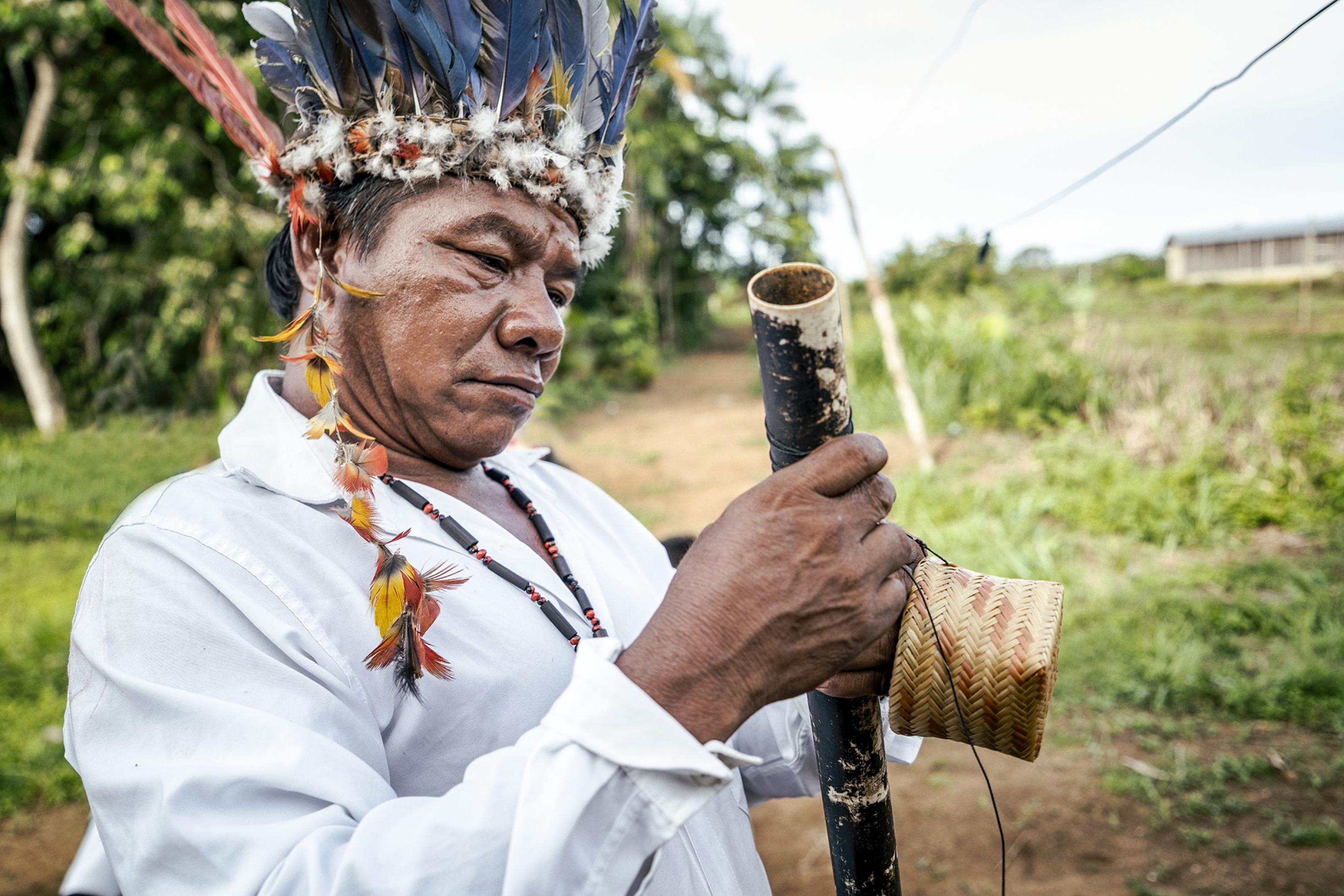 Ein indigener Mann mit Federkopfschmuck blickt prüfend auf ein Rohr.