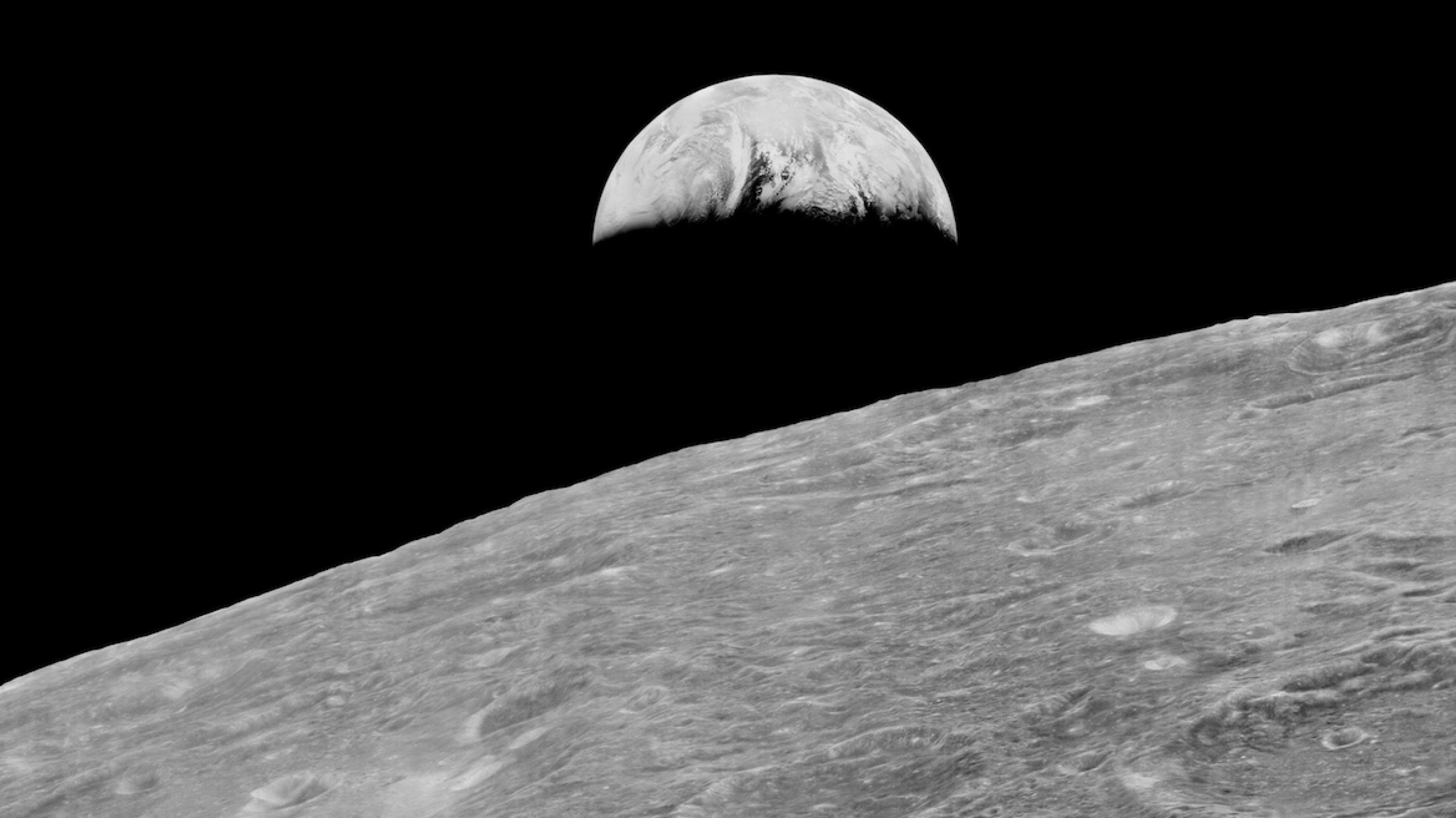 Schwarzweiß-Foto: Die angeschnittene Mondoberfläche, darüber die Erde mit gut erkennbaren Wolkenbändern. Es ist das erste Earth rise-Bild, aufgenommen vom Lunar Orbiter 1 der NASA im August 1966.