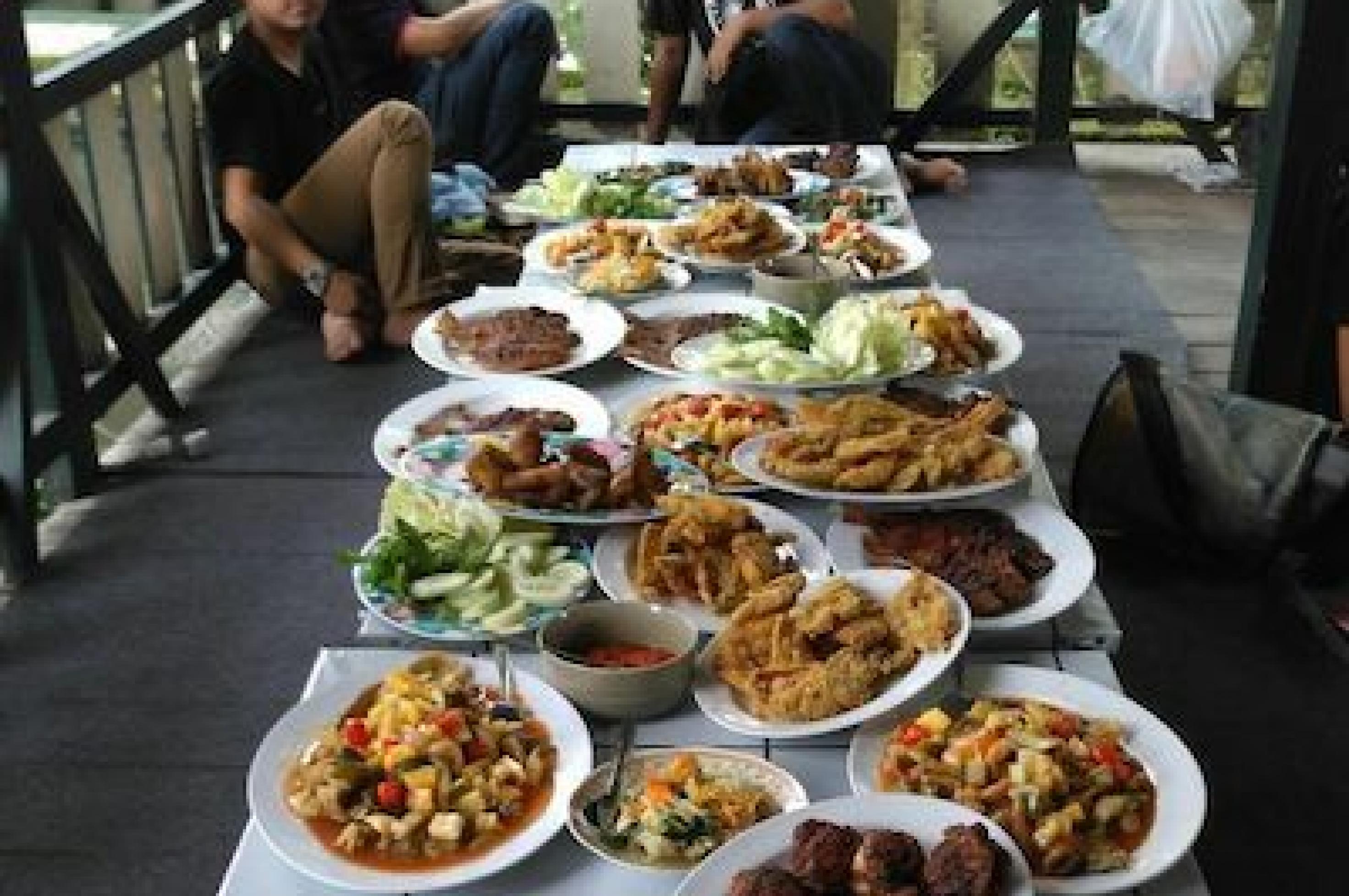 Viele Indonesier brechen das Fasten im Ramadan bei gemeinsamen Festessen. Ein langer Tisch, auf dem sich Teller gefüllt mit bunten Speisen von Gemüse über gebackenes und frittiertes Fleisch zu Käse türmen.