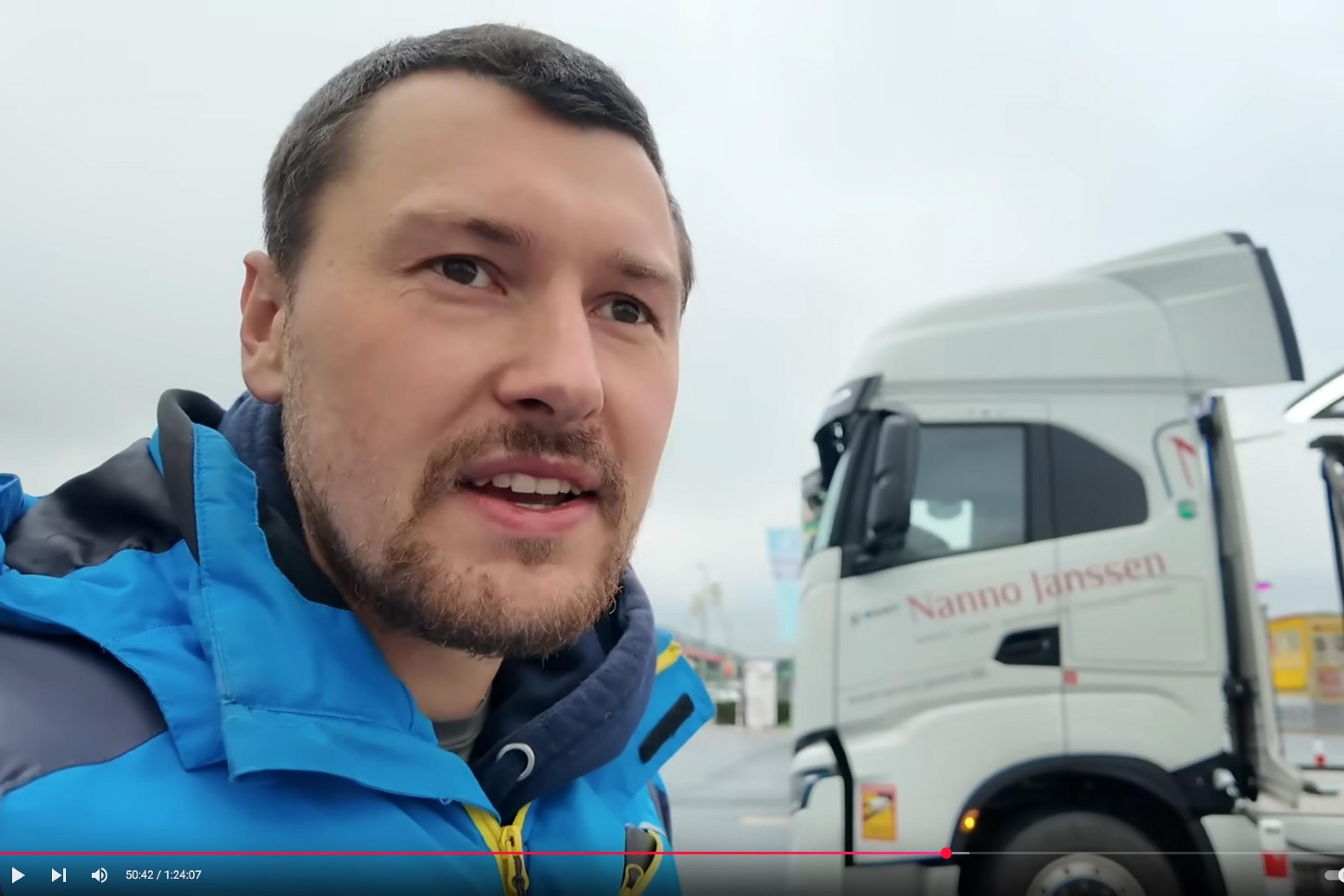 Ein junger Mann in blauer Winterjacke steht vor einer weißen Zugmaschine an einer Ladesäule