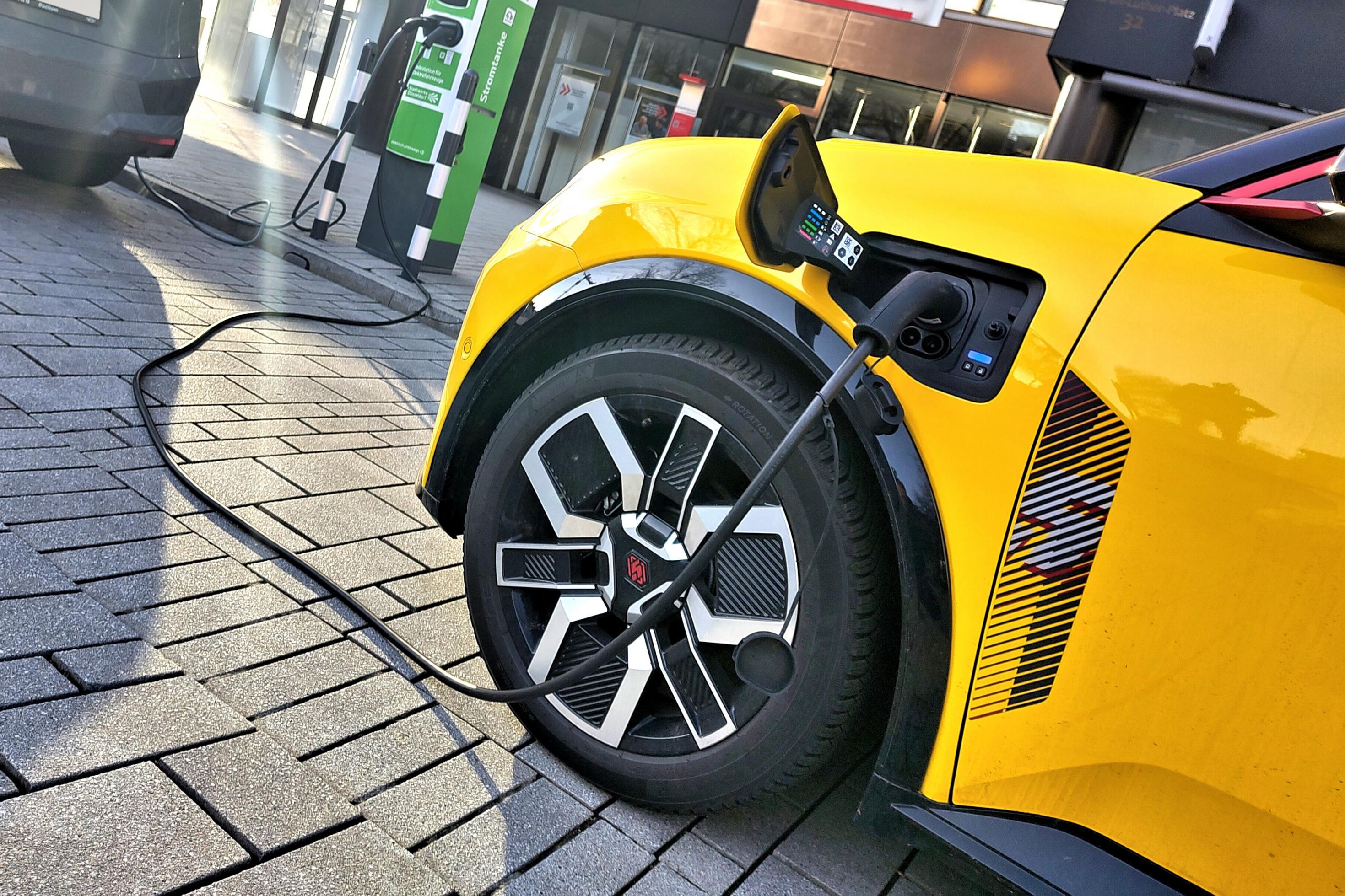 Ladekabel führt von einer Ladestation in die Anschlussbuchse eines gelben E-Autos.