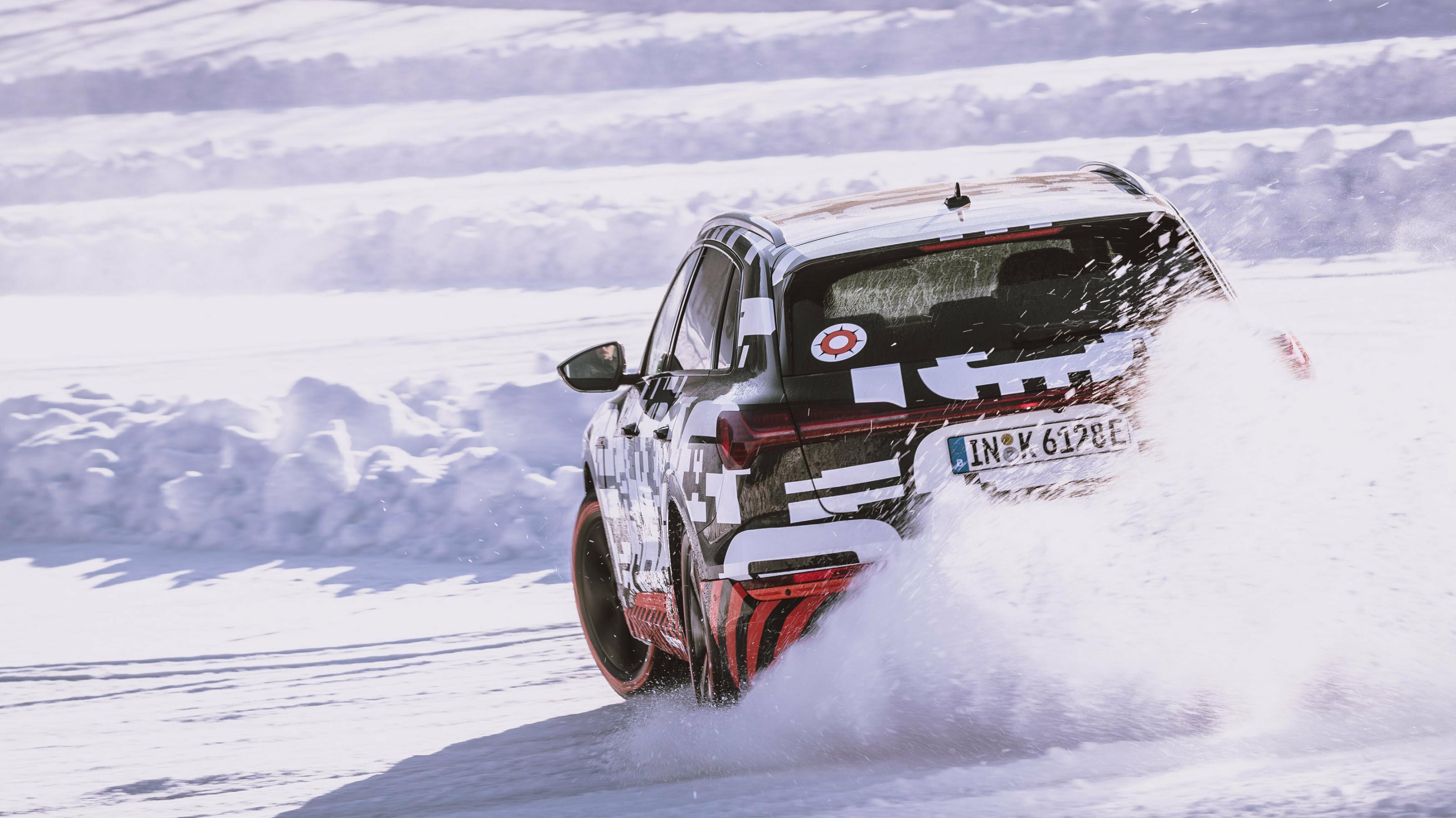 Ein mit Rallye-Muster beklebtes Elektroauto pflügt durch den Schnee. Die Aufnahme zeigt das Auto von hinten, wie es um die Kurve fährt und Schnee aufwirbelt.