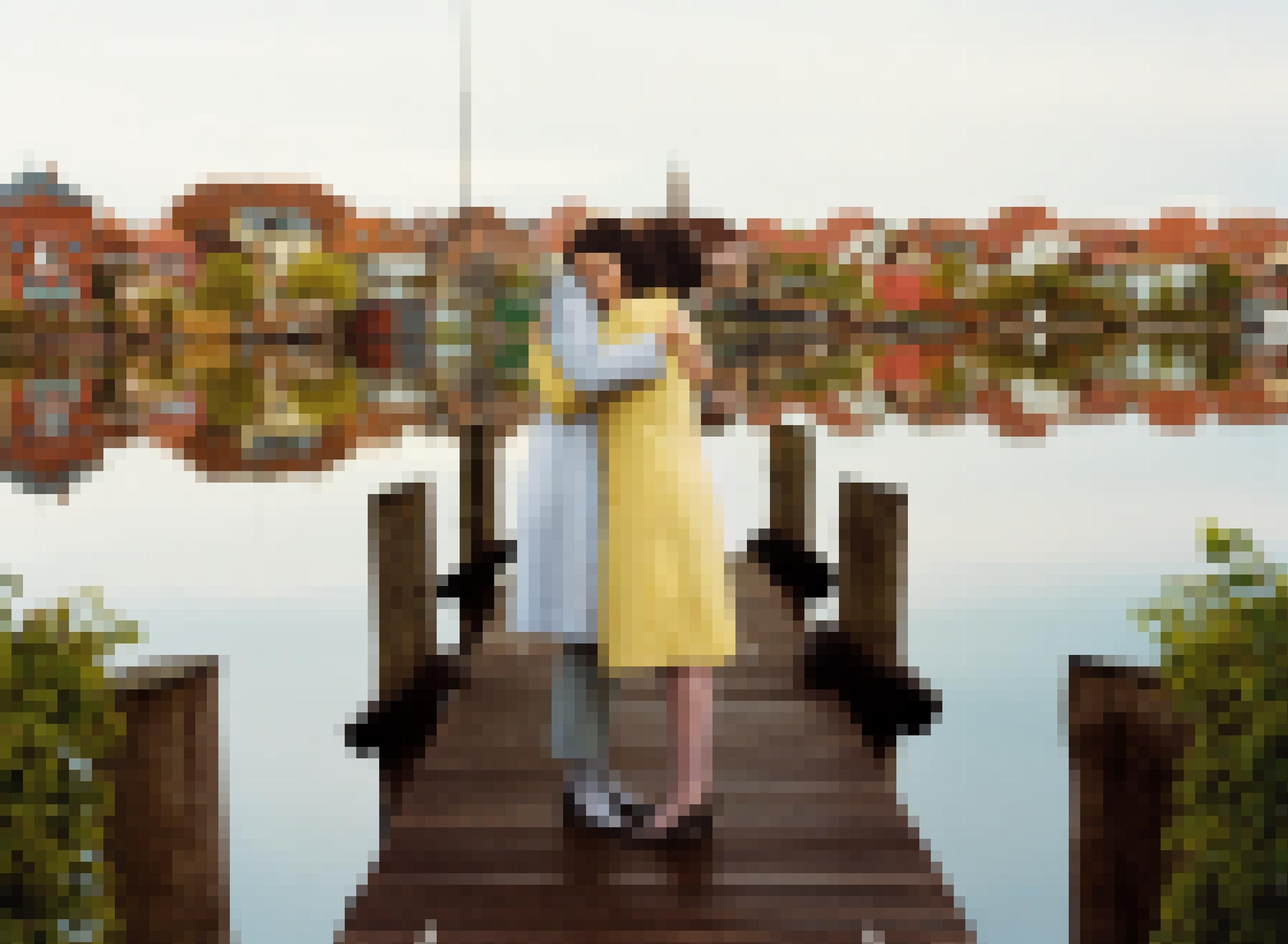 Zwei Frauen umarmen sich auf einem Steg. Im Hintergrund spiegeln sich die Häuser des Ortes im Wasser.