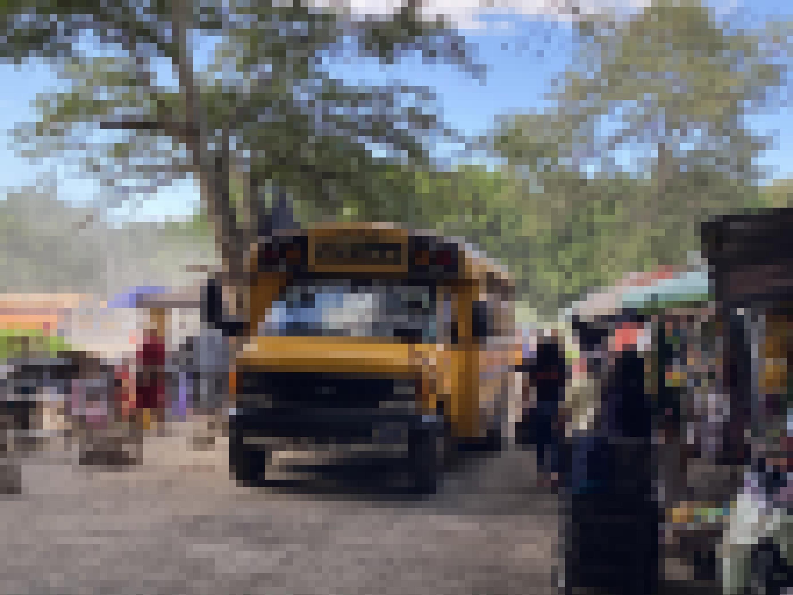Ein alter gelber US-Schulbus fährt auf einer ungeteerten, staubigen Piste an Marktständen vorbei.