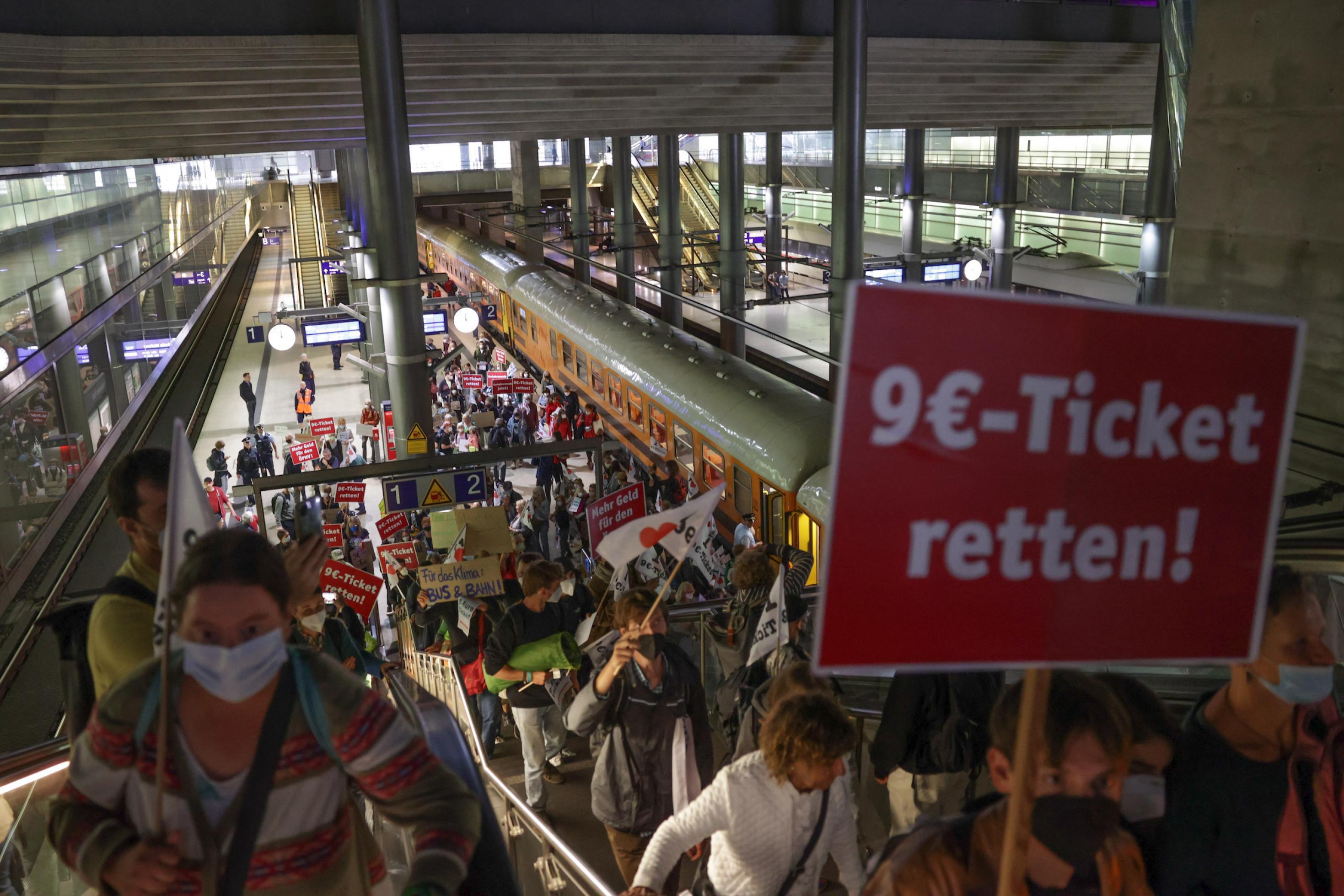 Aus einer Menschenmange am Bahnhof ragt ein Schild „9 Euro Ticket retten“.