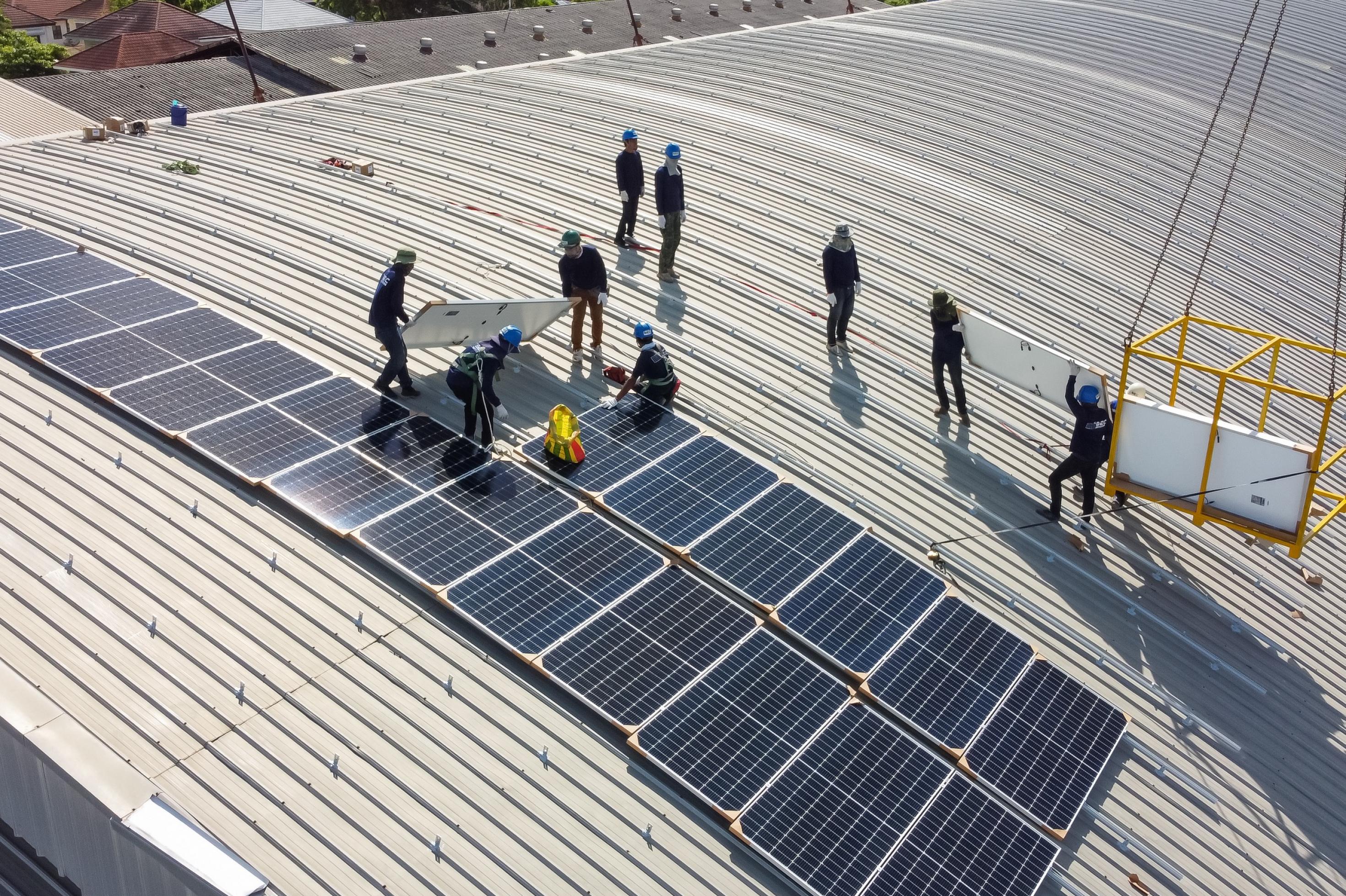 Installateure auf dem Dach einer Fabrik installieren Solarpanele.