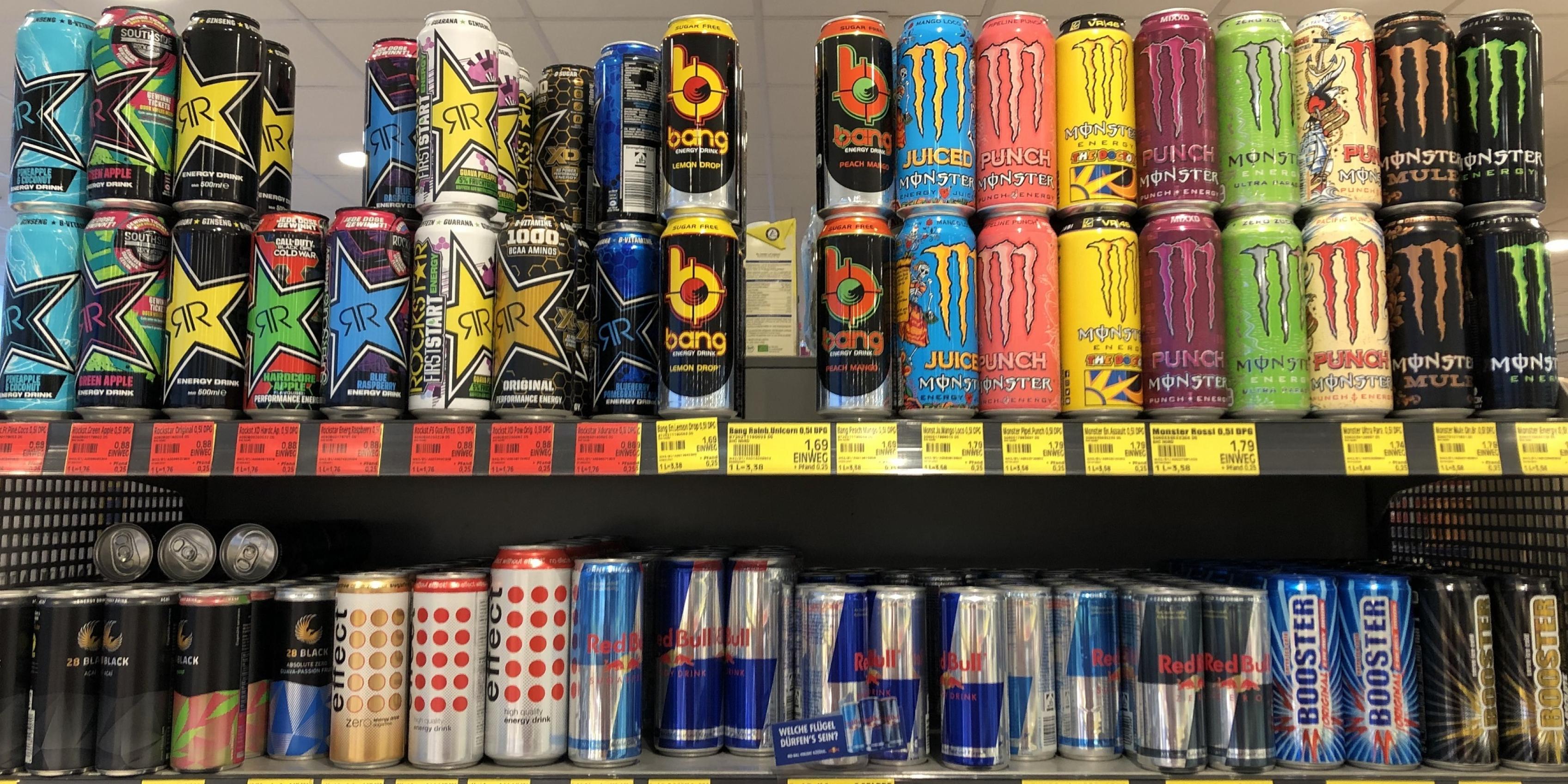 Zwei Supermarktregale sind voll mit vielen bunten Getränkedosen. Es sind Energy-Drinks verschiedener Hersteller und Geschmacksrichtungen.