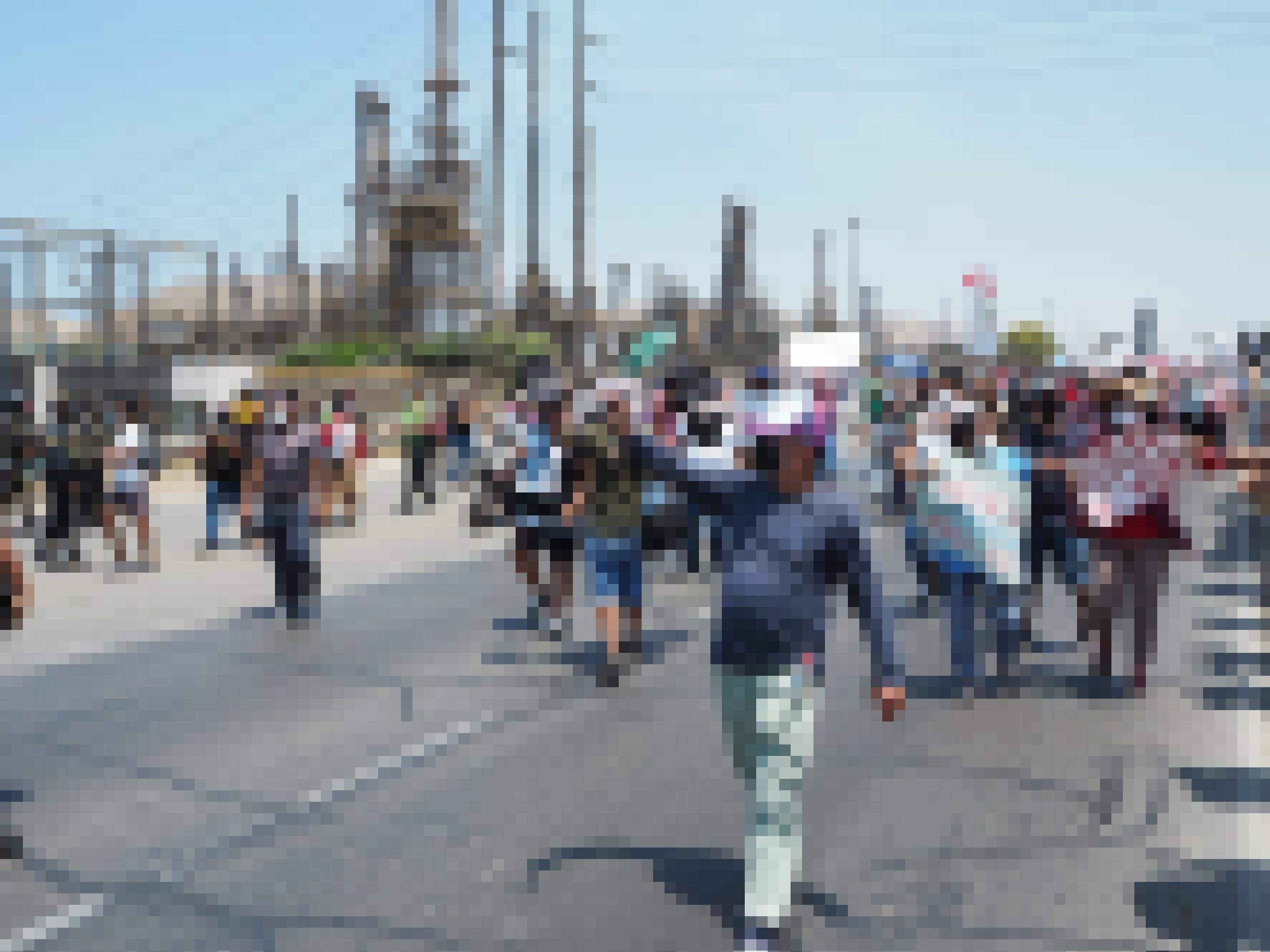 Menschen protestieren mit Plakaten auf einer Strasse, im Hintergrund sieht man eine Industrieanlage, eine Raffinerie.