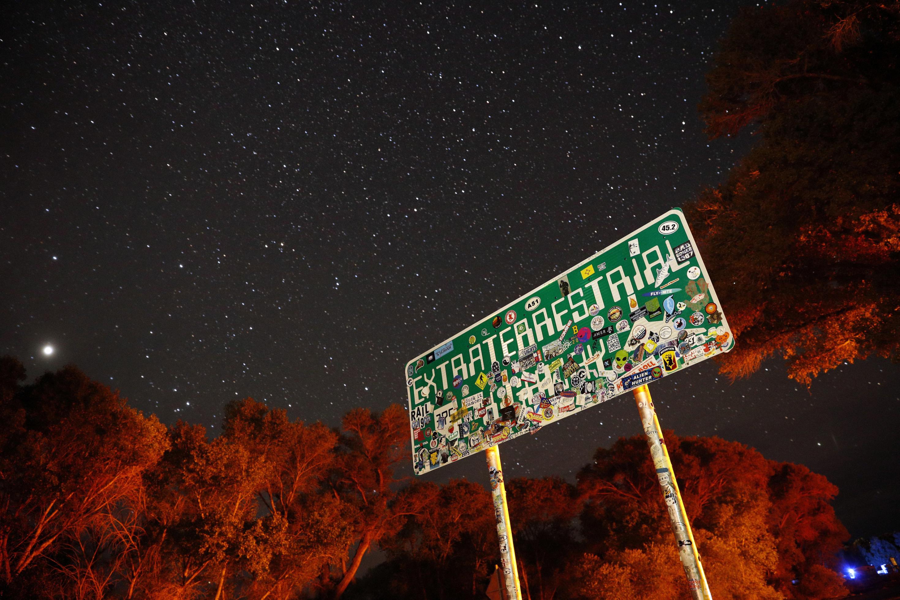 Ein mit Aufklebern überklebtes Schild mit der Aufschrift „Extraterrestrial Highway“ steht nachts unter einem Sternenhimmel.