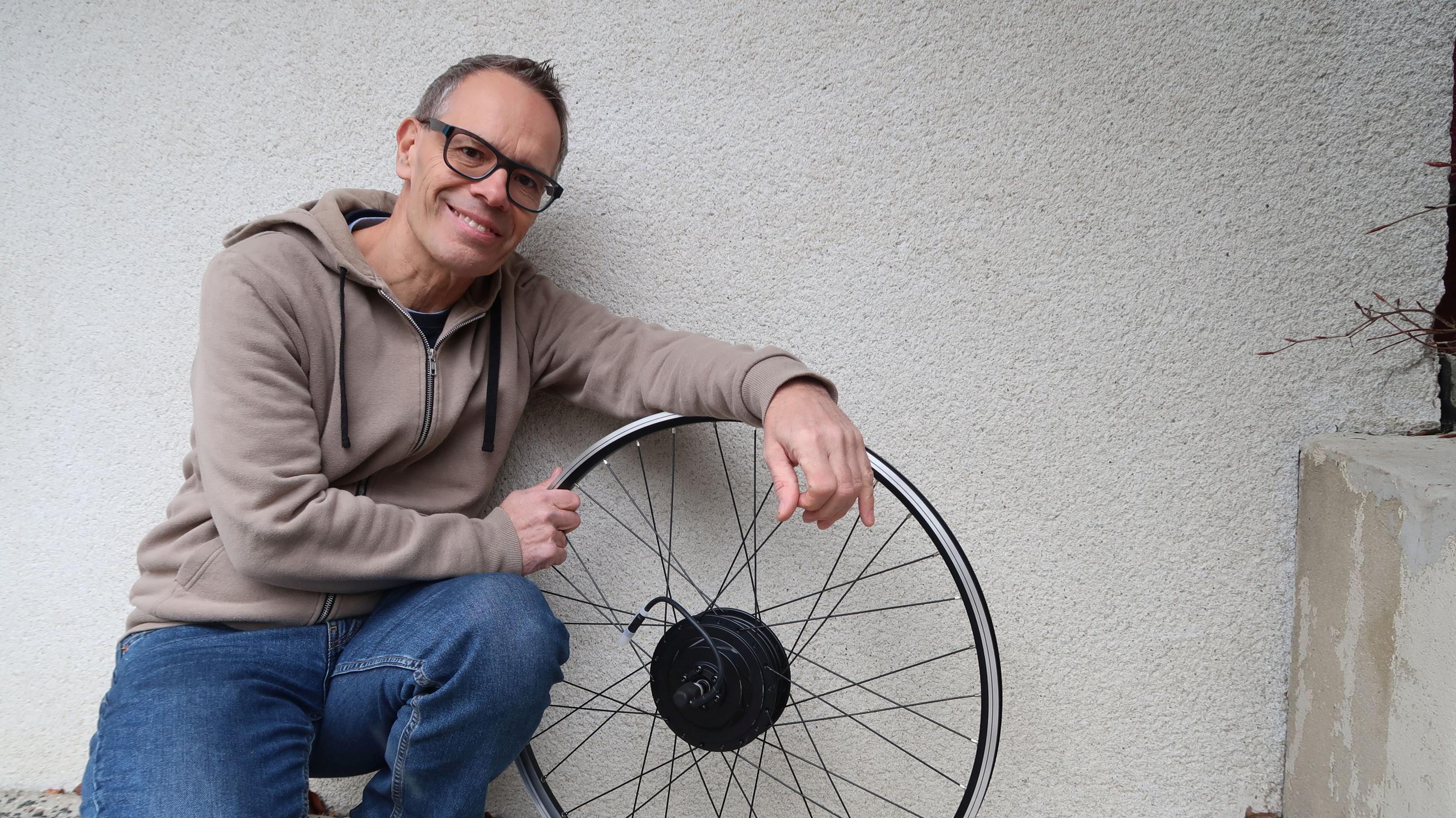 Hans Leitgeb hockt mit einem Fahrrad-Reifen an der Wand.