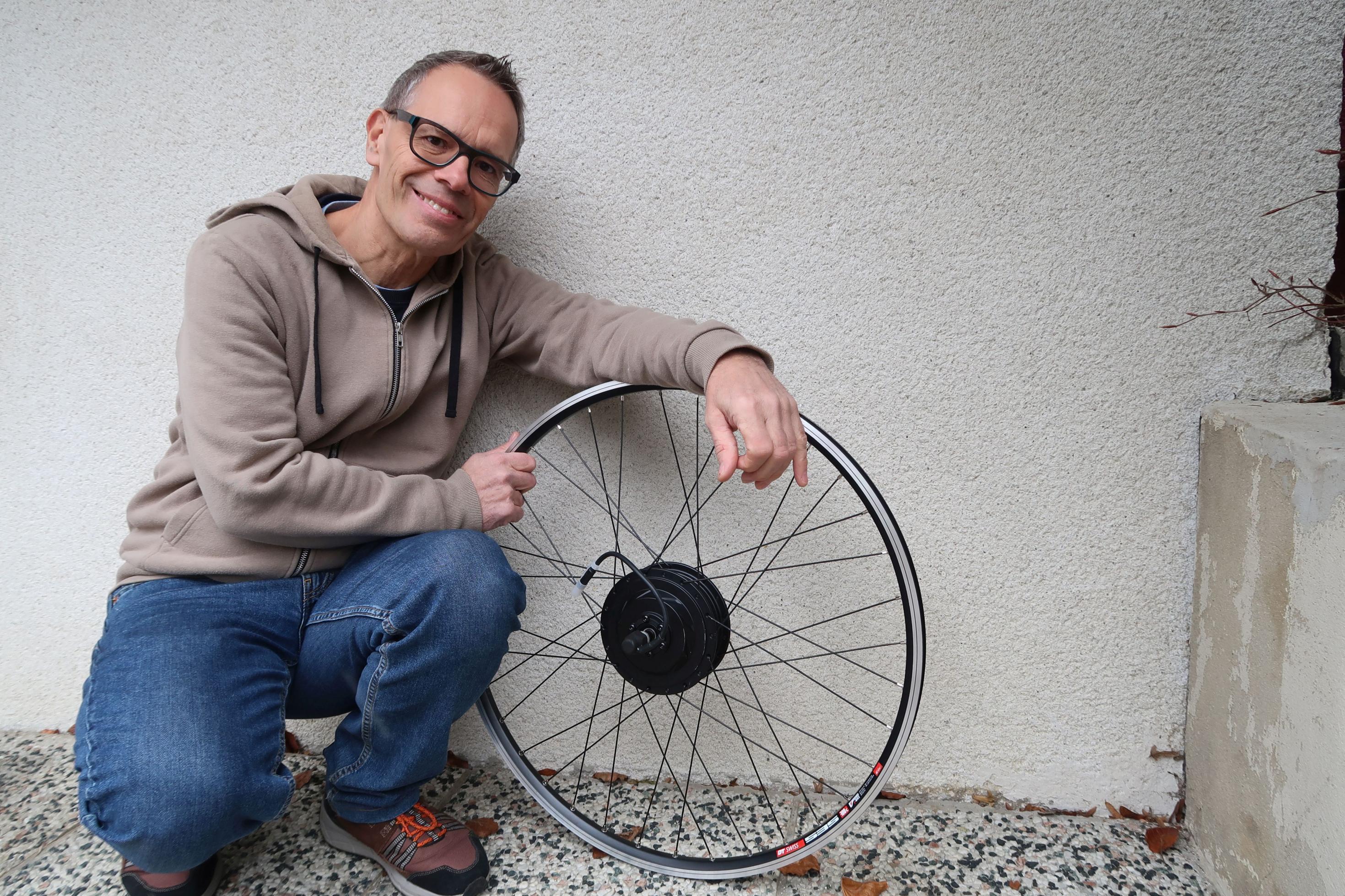 Hans Leitgeb hockt mit einem Fahrrad-Reifen an der Wand.