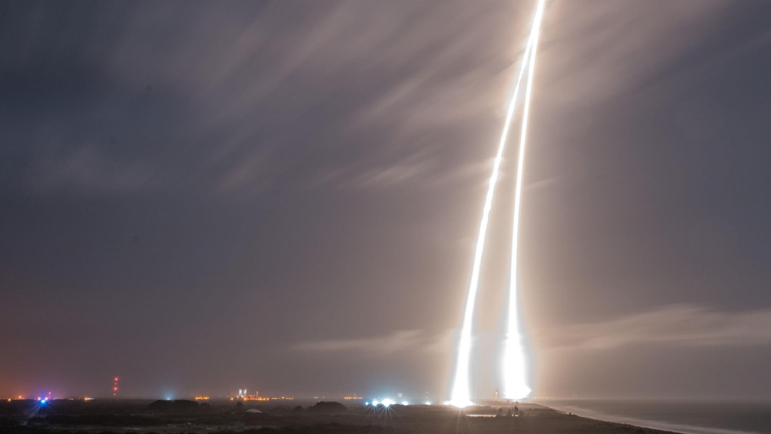 Die Langzeitaufnahme zeigt einen spitzen zweiseitigen Lichtstrahl am Himmel, der entstand, als eine Falcon-Rakete startete und später die Erststufe wieder landete.