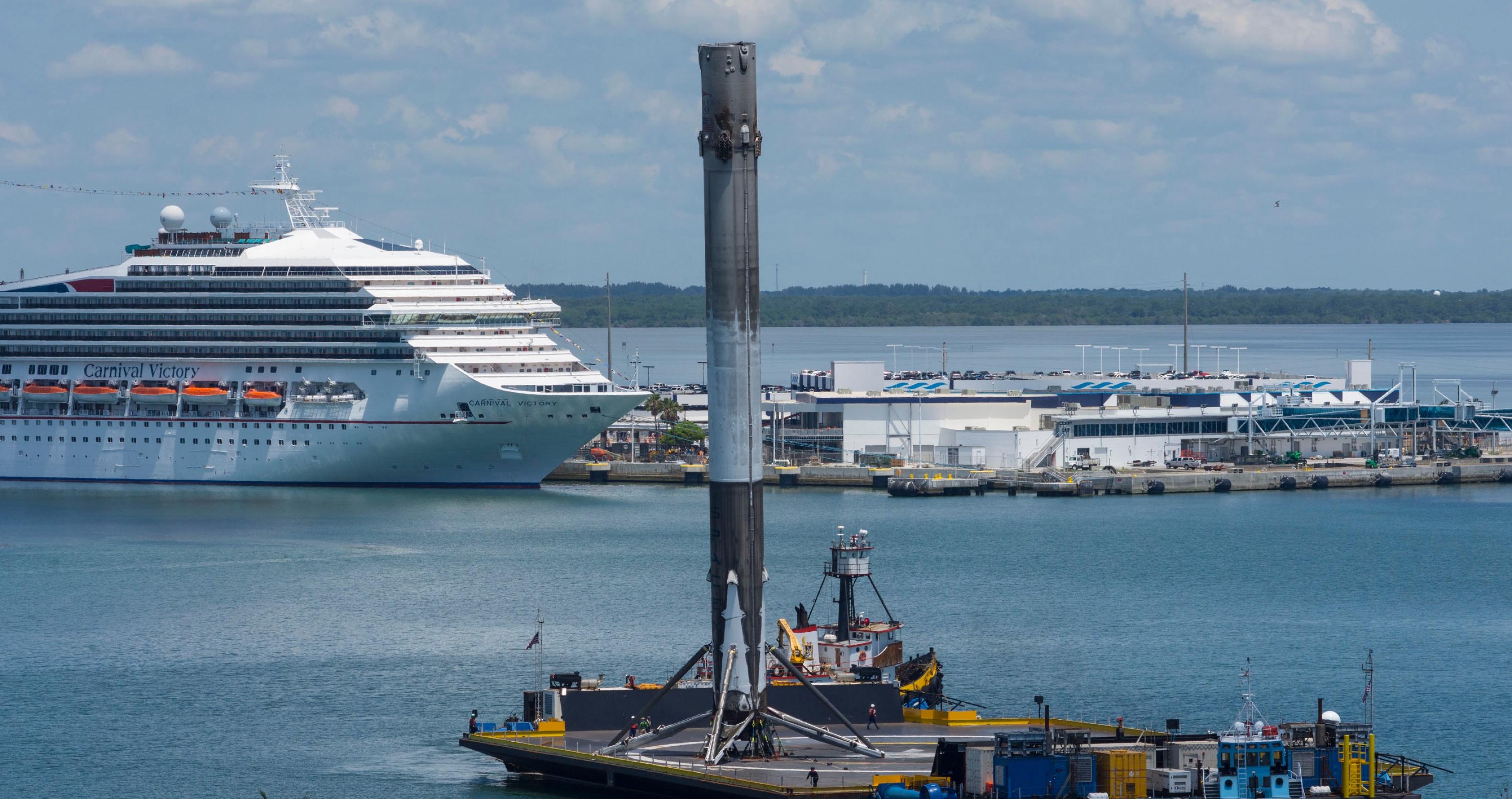 In einen Hafen fährt das Drohnenschiff mit einem zuvor gelandeten und ausgebrannten Booster der Falcon-9-Rakete ein.