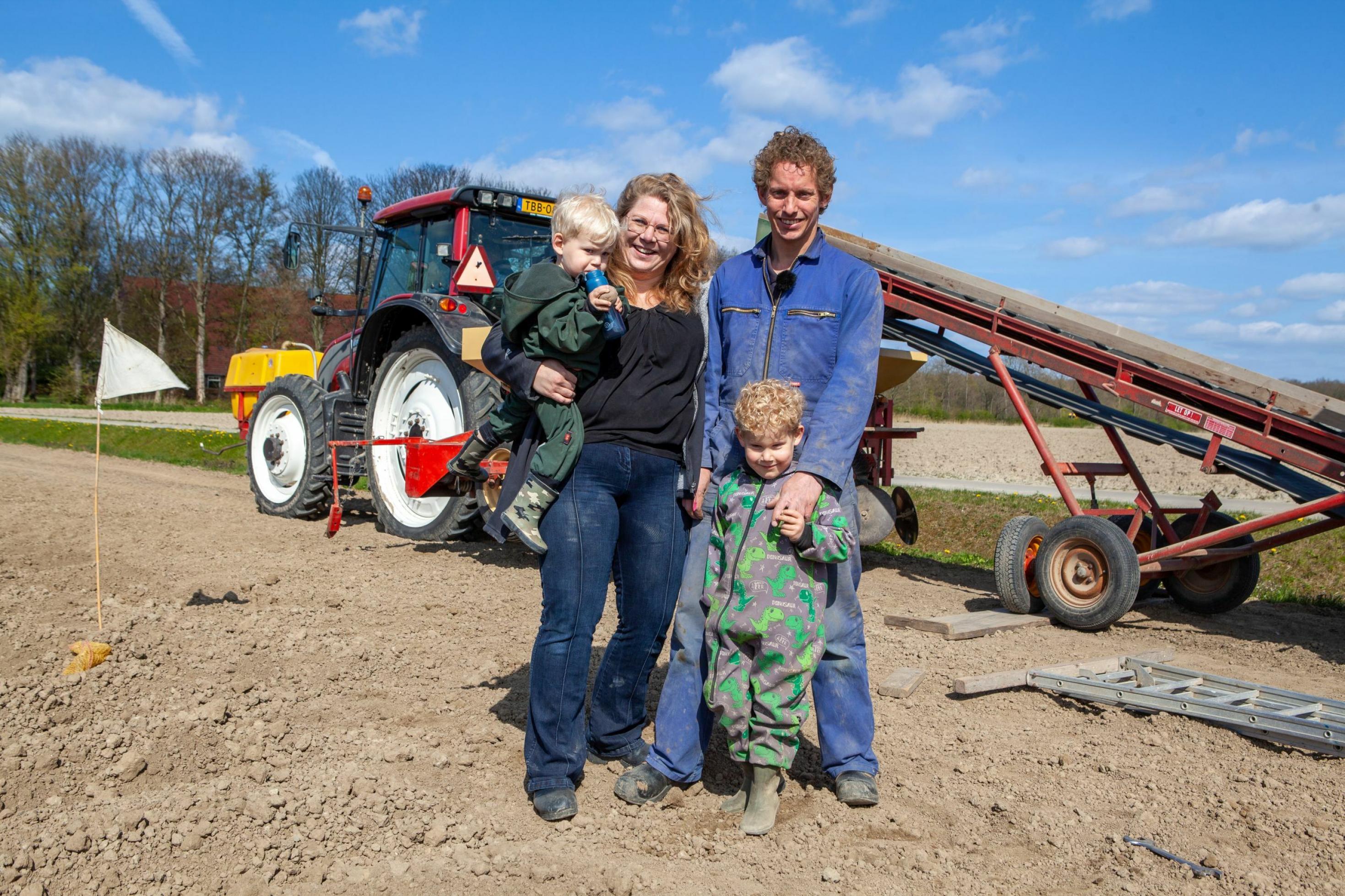 Vierköpfige Familie – Vater, Mutter, zwei blondgelockte kleine Buben – stehen auf dem Acker und blicken in die Kamera. Im Hintergrund ein Traktor mit einem Anhänger.