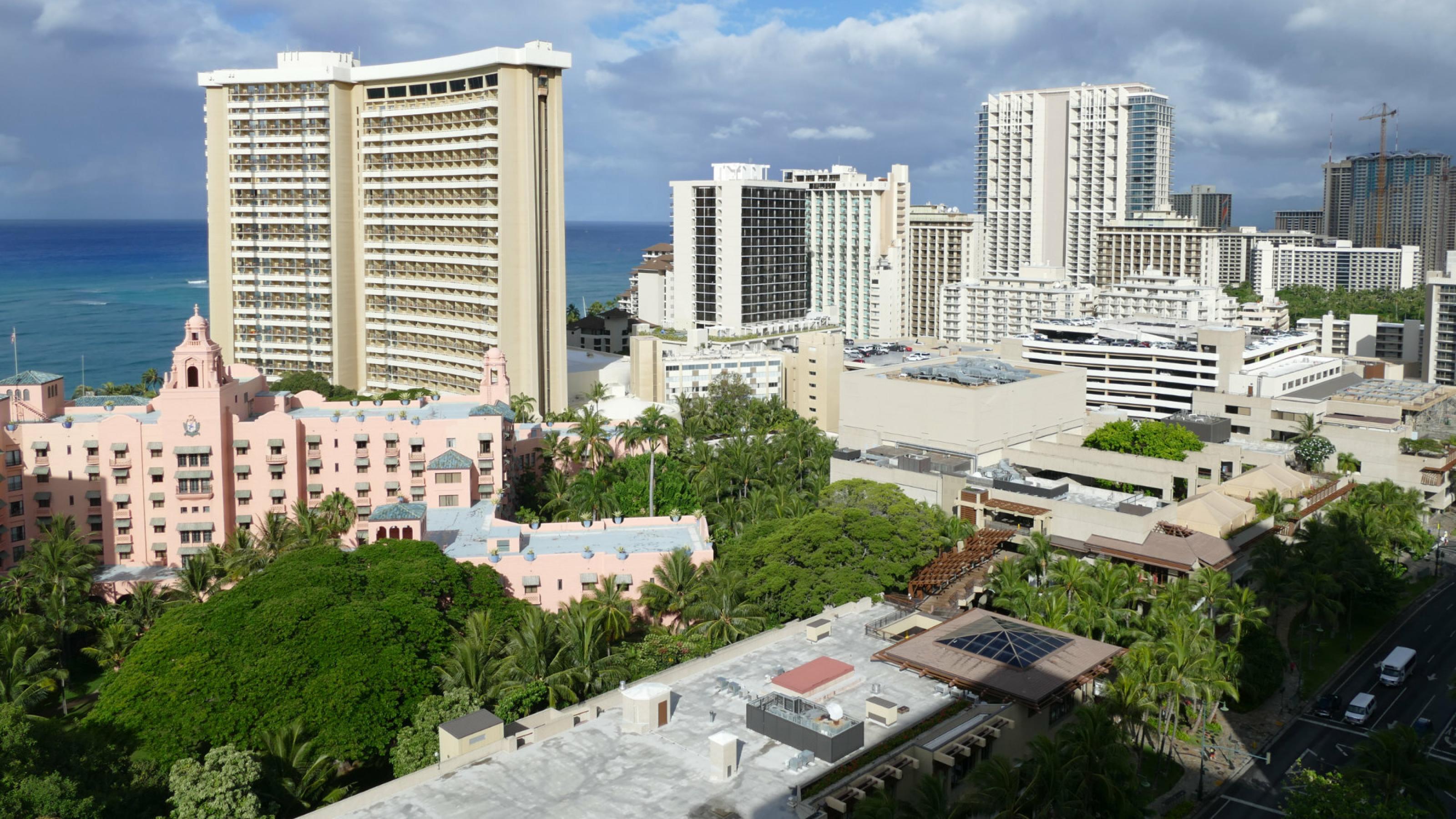Stadtviertel von Honolulu mit Hochhäusern am Meer, zwischen den Gebäuden stehen Bäume und Palmen.