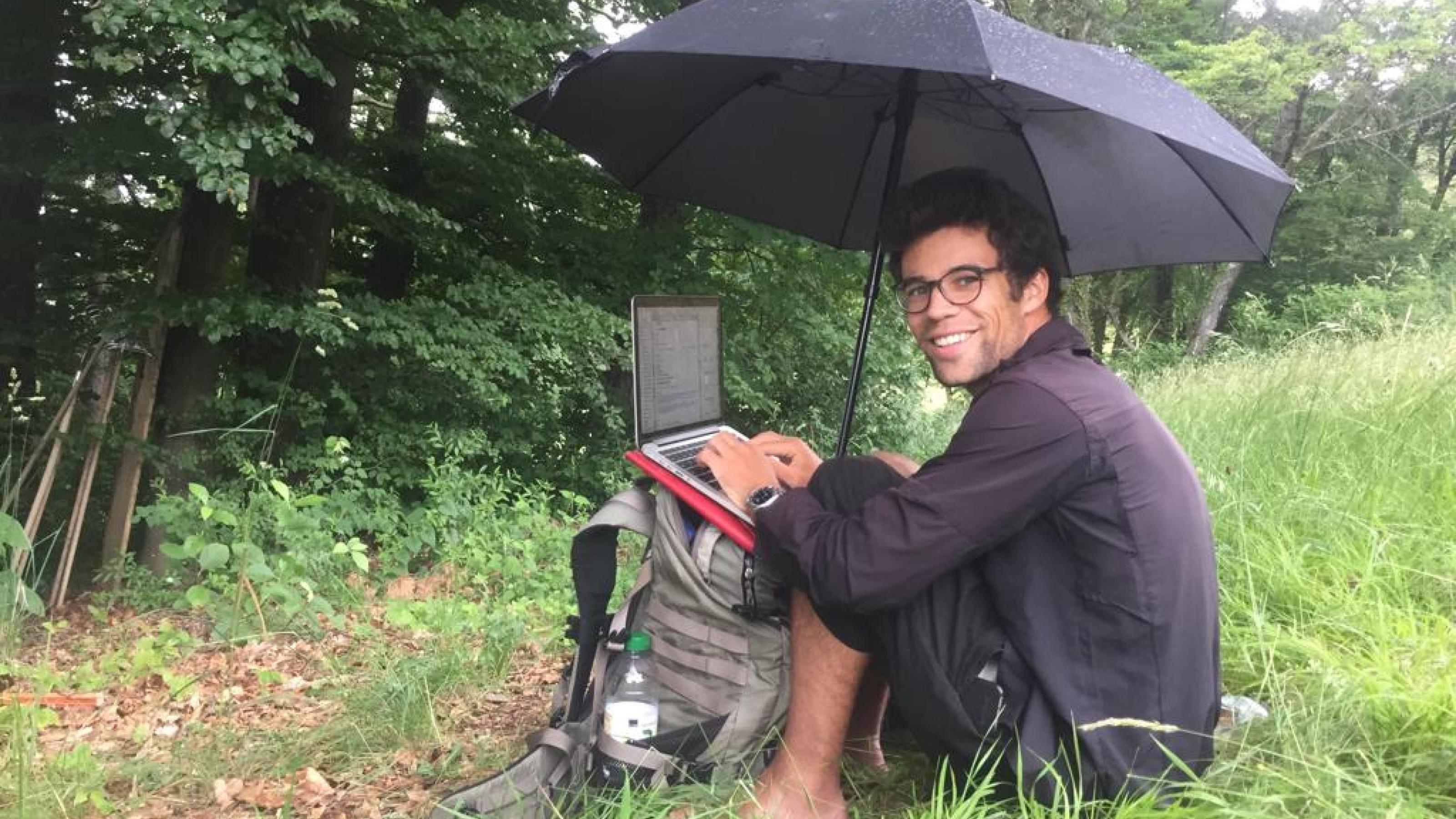 ein Mann sitzt unter einem Regenschirm und benutzt einen Laptop [AI]