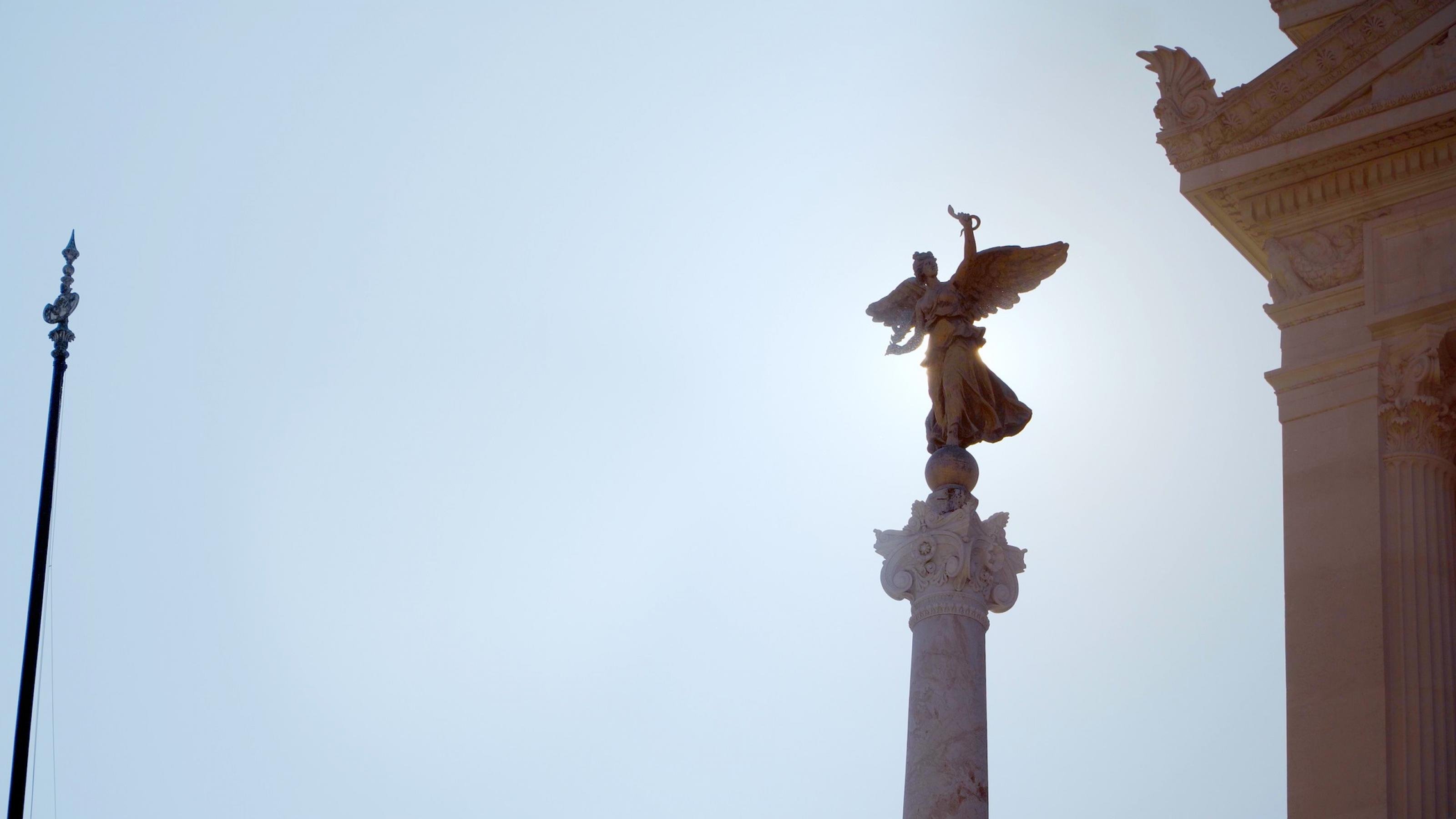 Blauer Himmel, in den eine hohe Skulpturensäule mit der Figur einer Göttin ragt sowie ein Stück eines barocken Gebäudes.