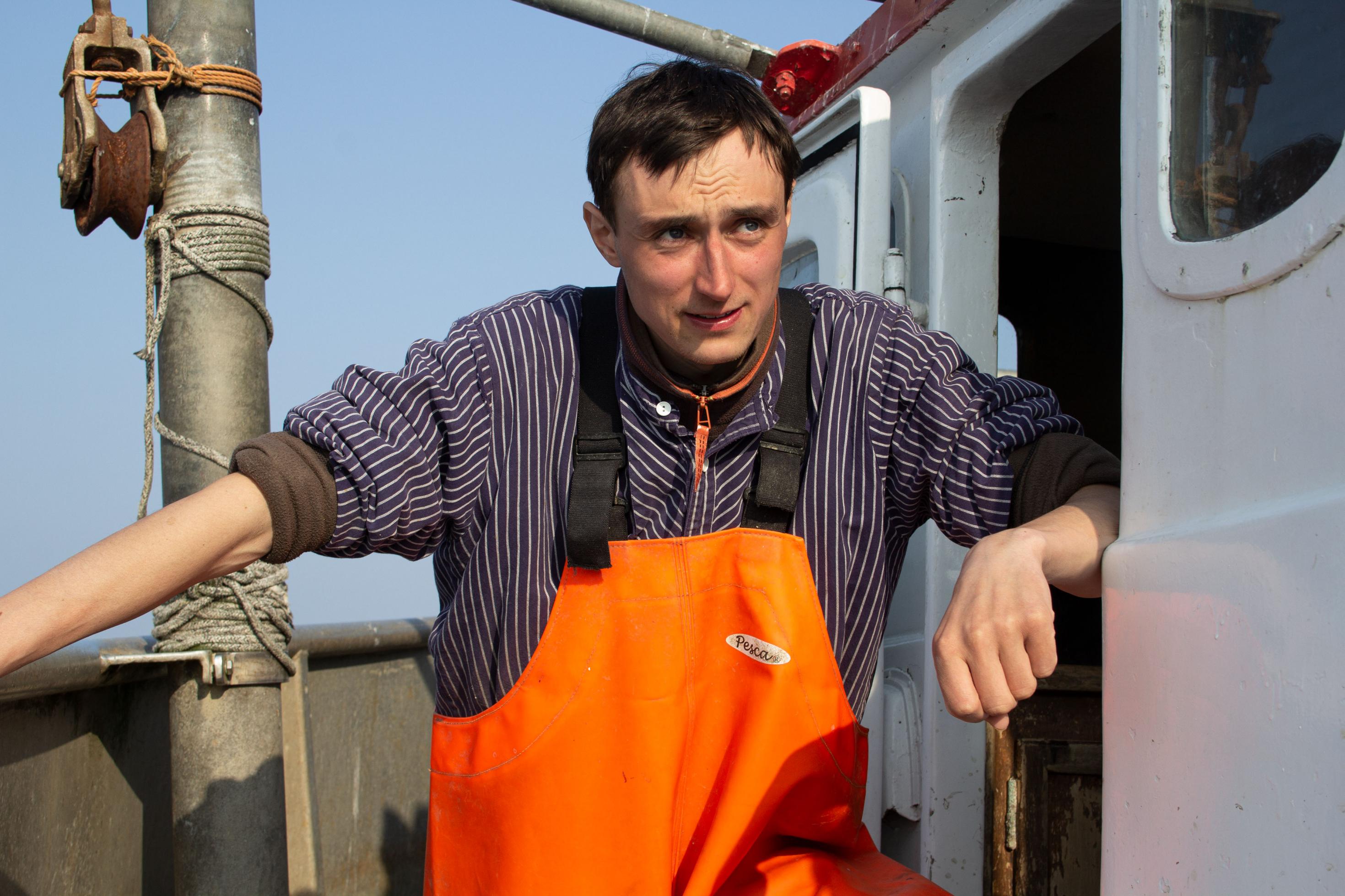 Portrait Fischer in gestreiftem Hemd und oranger Wathose.