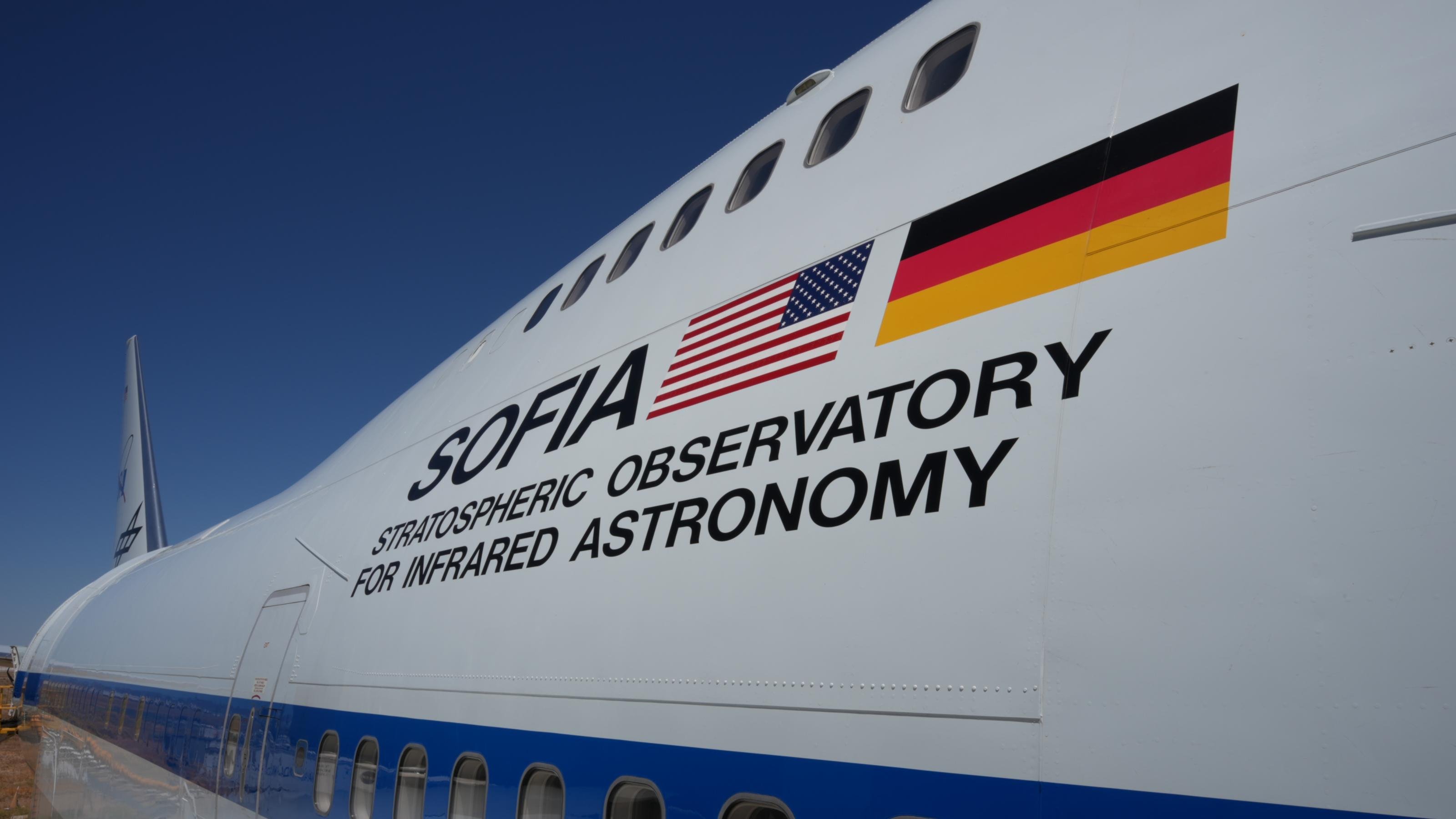 SOFIA, das fliegende Observatorium in einem umgebauten Jumbo-Jet steht zum Abflug bereit auf der Rollbahn. Neben dem Eingang sind die deutsche und die US-Flagge aufgeklebt sowie der Schriftzug: STRATOSPHERIC OBSERVATORY FOR INFRARED ASTRONOMY.