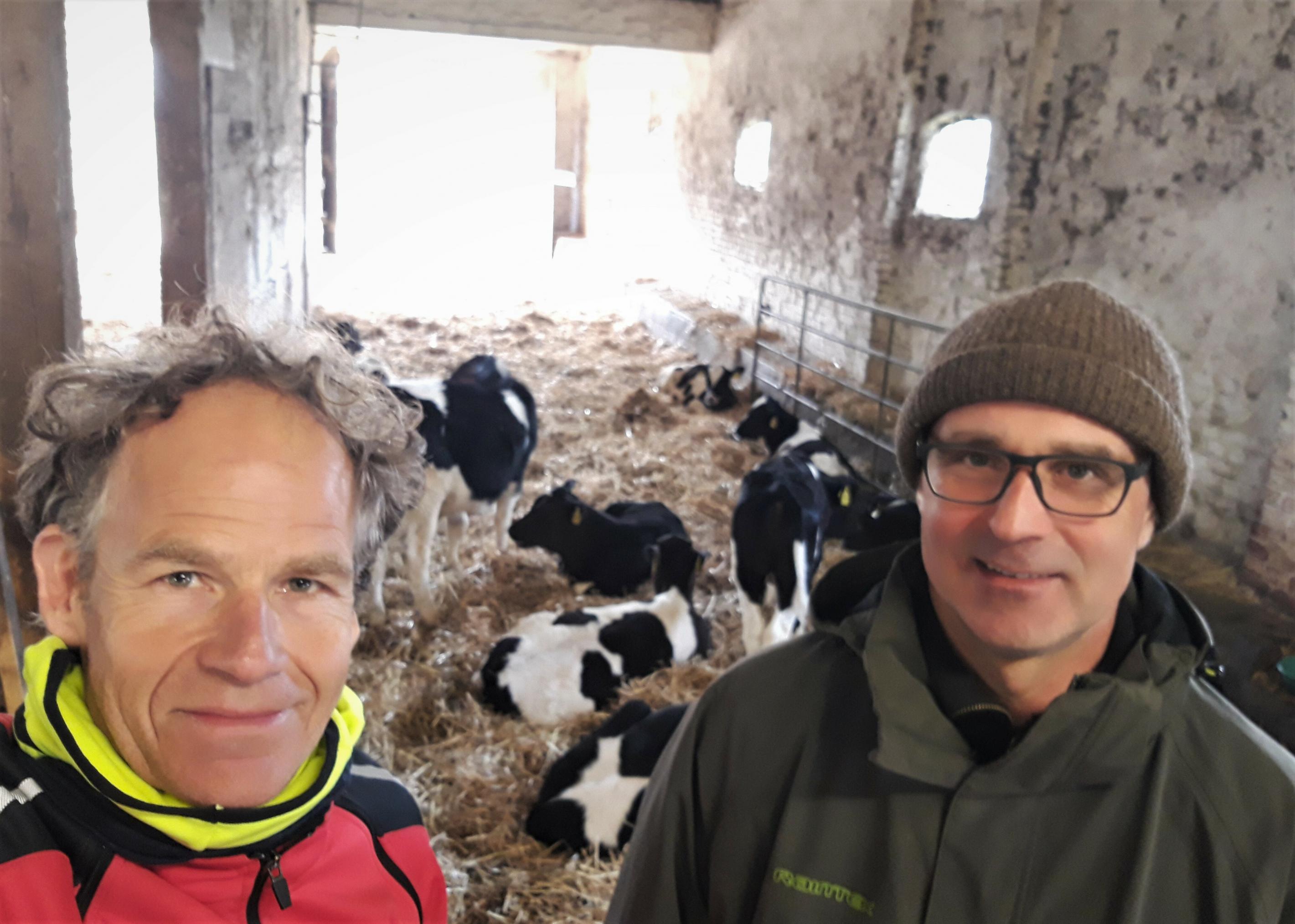 Der Landwirt und der RadelndeReporter äugen in die Kamera. Die meisten Kälber im Hintergrund ruhen auf der Strohunterlage.