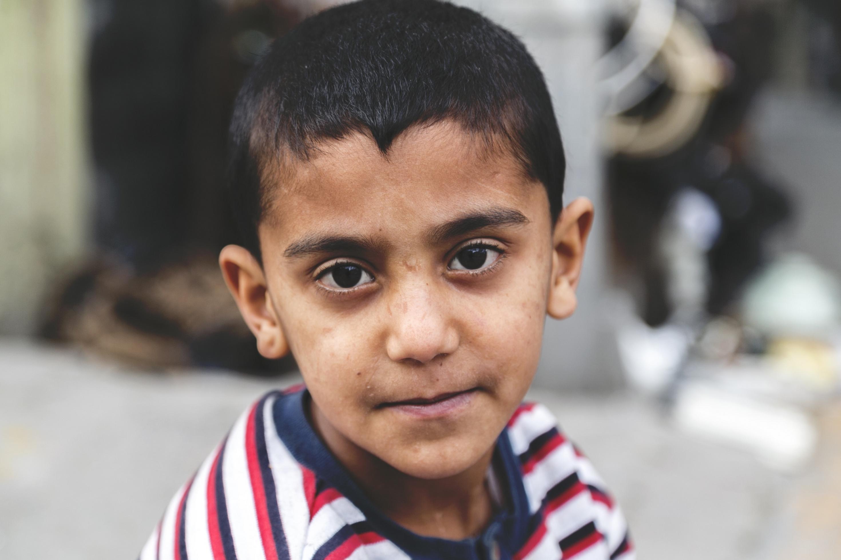 Ein kleiner Junge mit gestreiftem T-Shirt und kurzen dunklen Haaren schaut mit traurigen großen braunen Augen direkt in die Kamera.