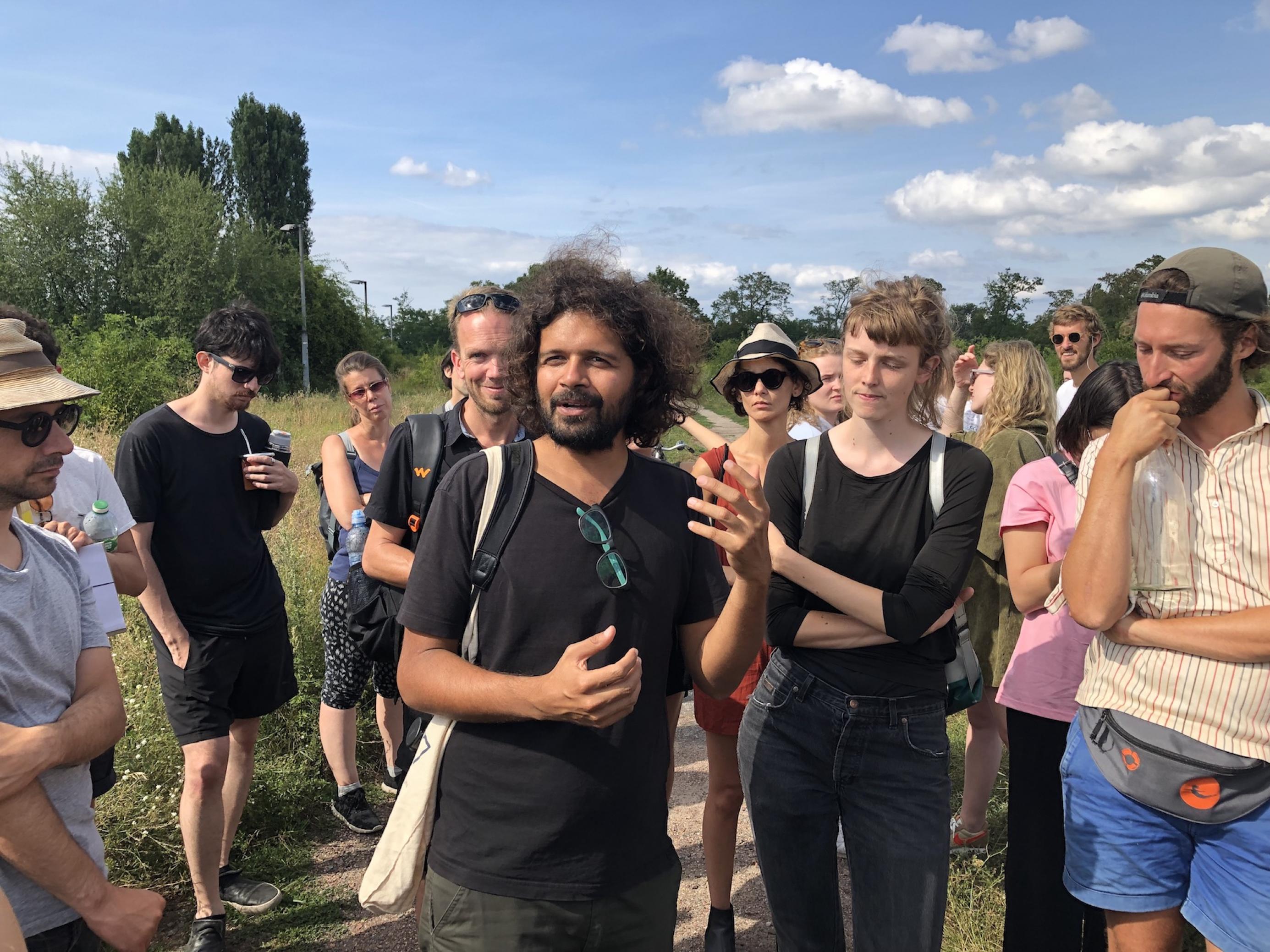 Hemal Naik leitet eine Vogelexkursion im Sommer in Berlin. Um ihn herum stehen viele Menschen in sommerlicher Kleidung.