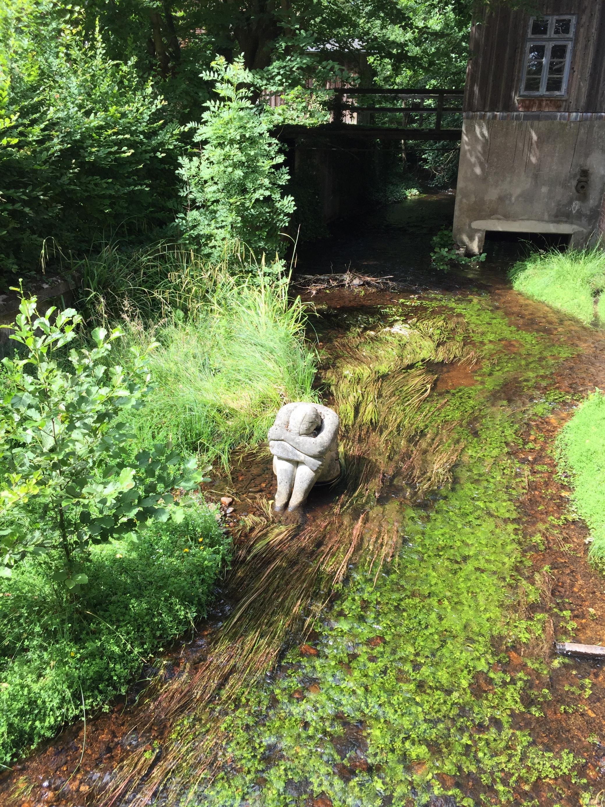 Im Bachbett der Lutter, die nicht weit von Celle an einer Mühle vorbeifließt, sitzt die Heide aus Lüneburg – eine Steinskulptur der Künstlerin Petra Förster