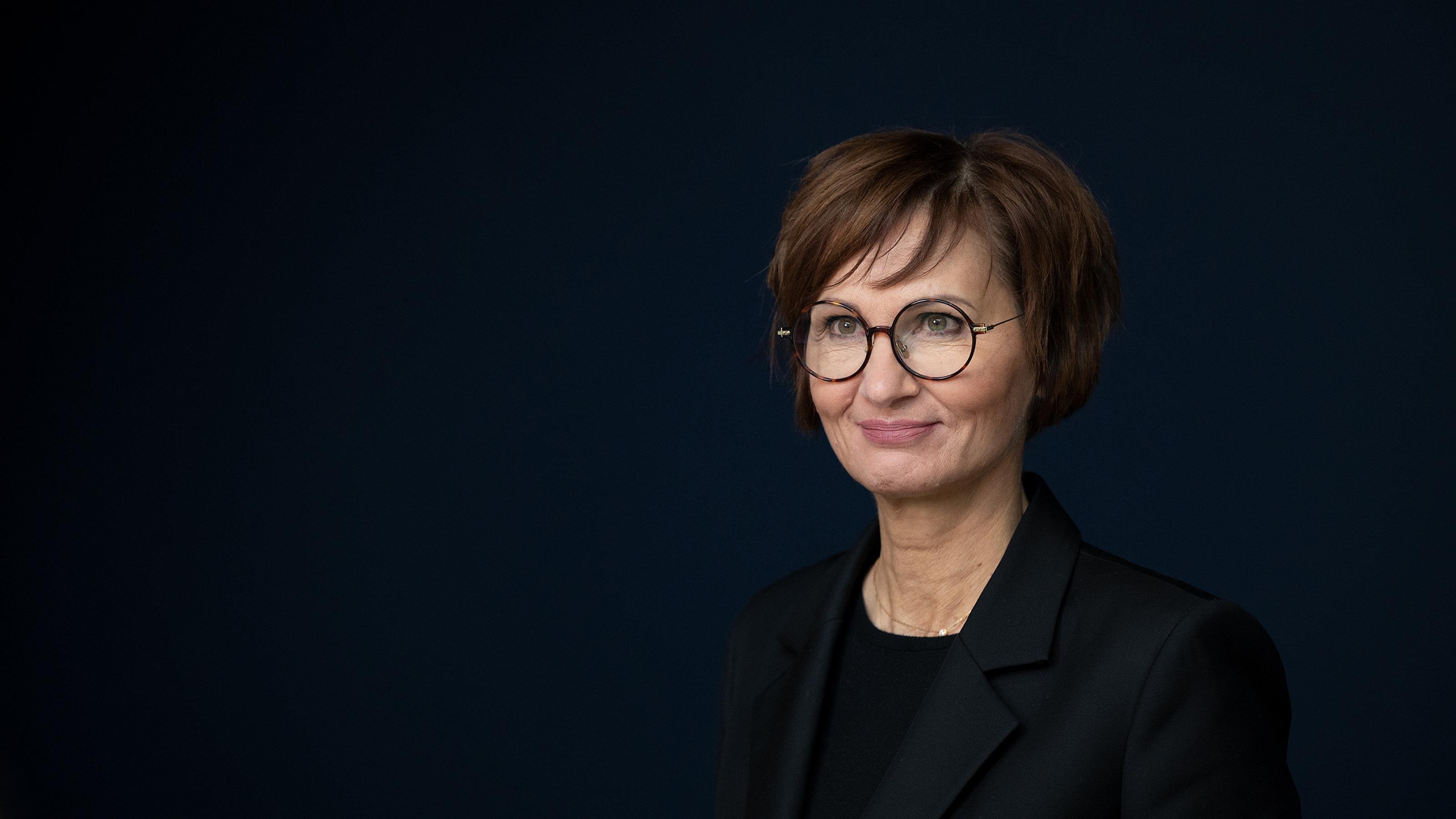 Portrait von Bundesforschungsministerin Bettina Stark-Watzinger vor sehr dunklem, blauem Hintergrund.