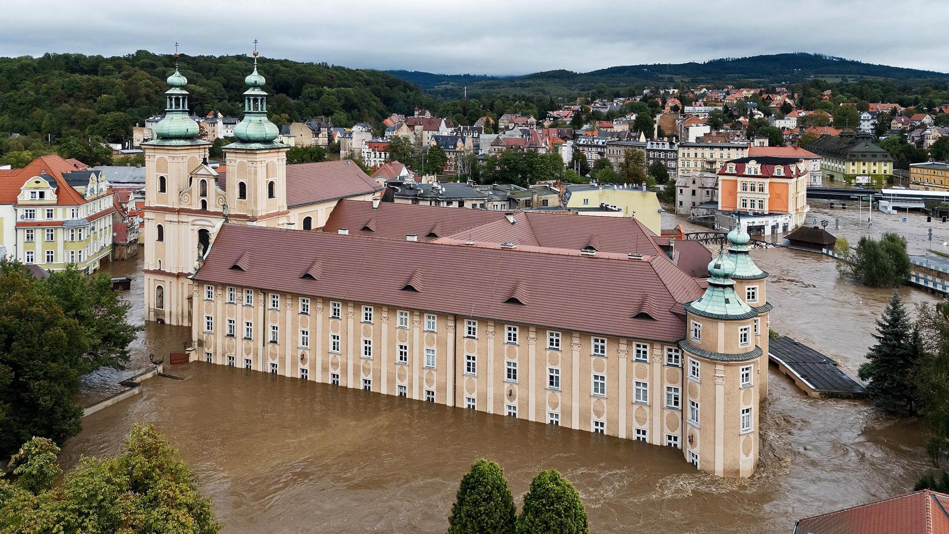 Luftbild eines großen Klostergebäüdes mit weiteren Gebäuden im Hintergrund. Das Kloster steht mehrere Meter tief im Wasser einer Überschwemmung.