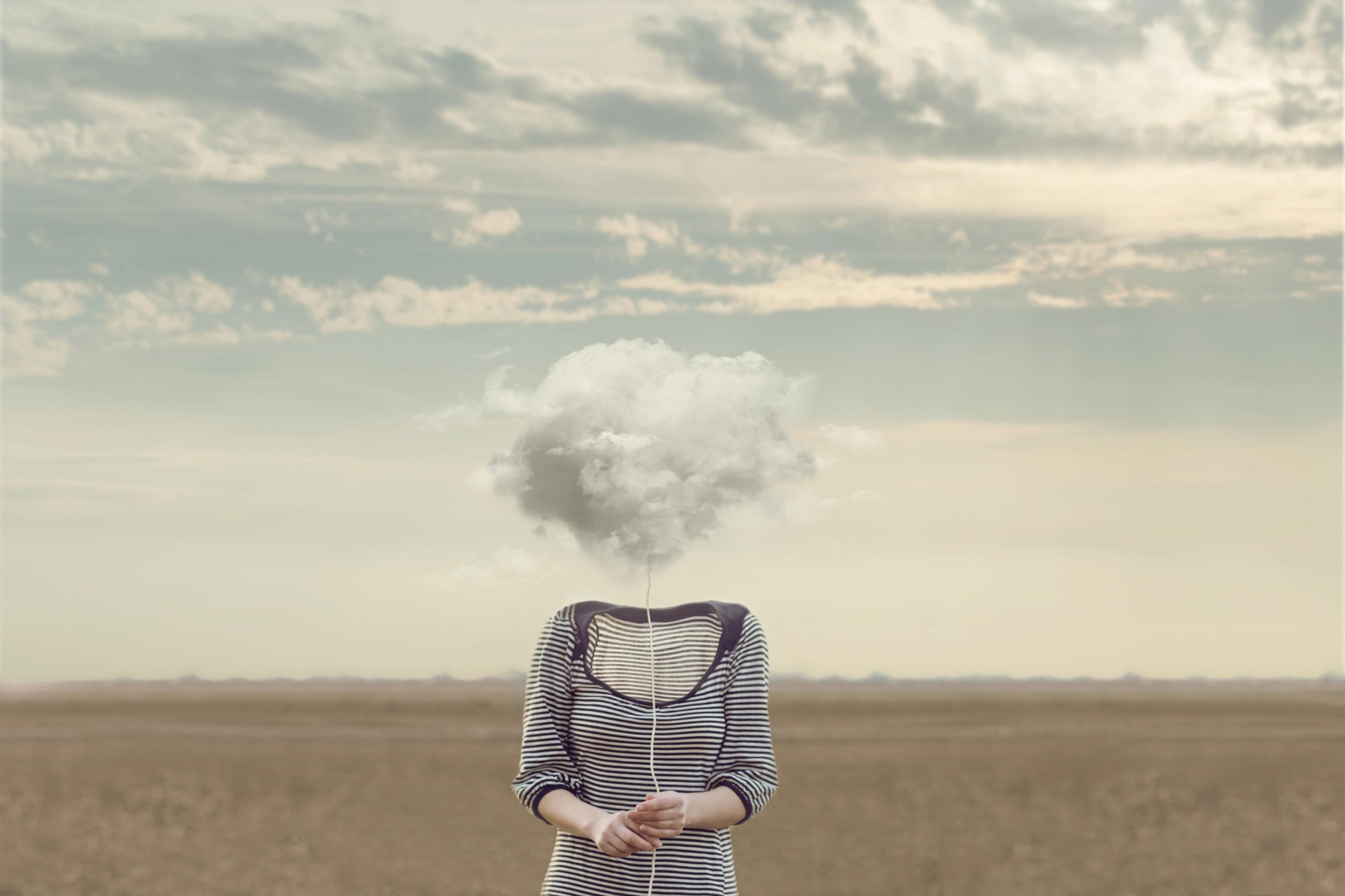 Eine Frau in einem grau-weiß gestreiften Kleid, steht ohne Kopf in einer Wüste. Anstelle ihres Kopfes ist eine Wolke abgebildet.