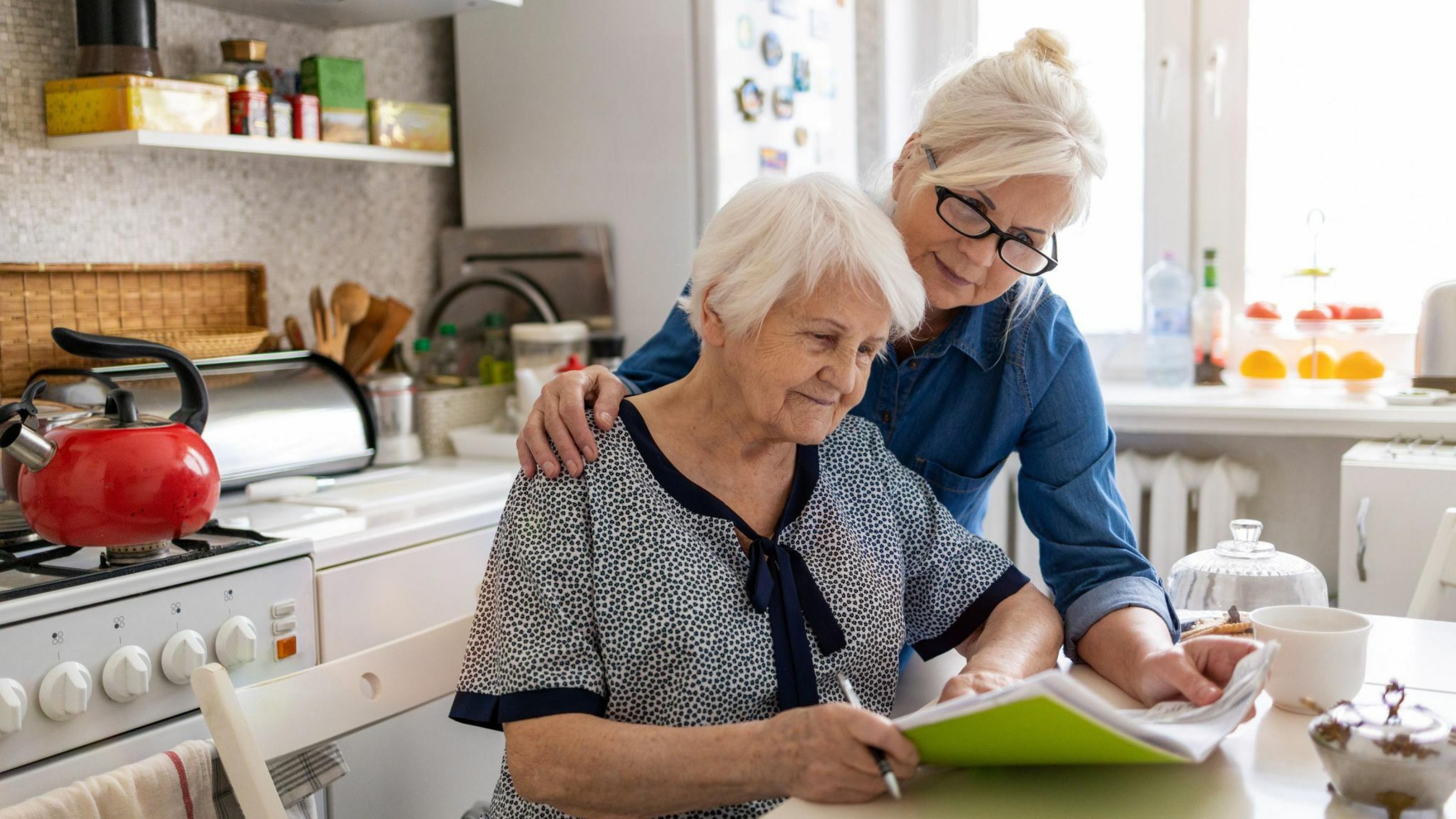 Eine Frau hilft ihrer alten Mutter am Küchentisch mit Papierkram.