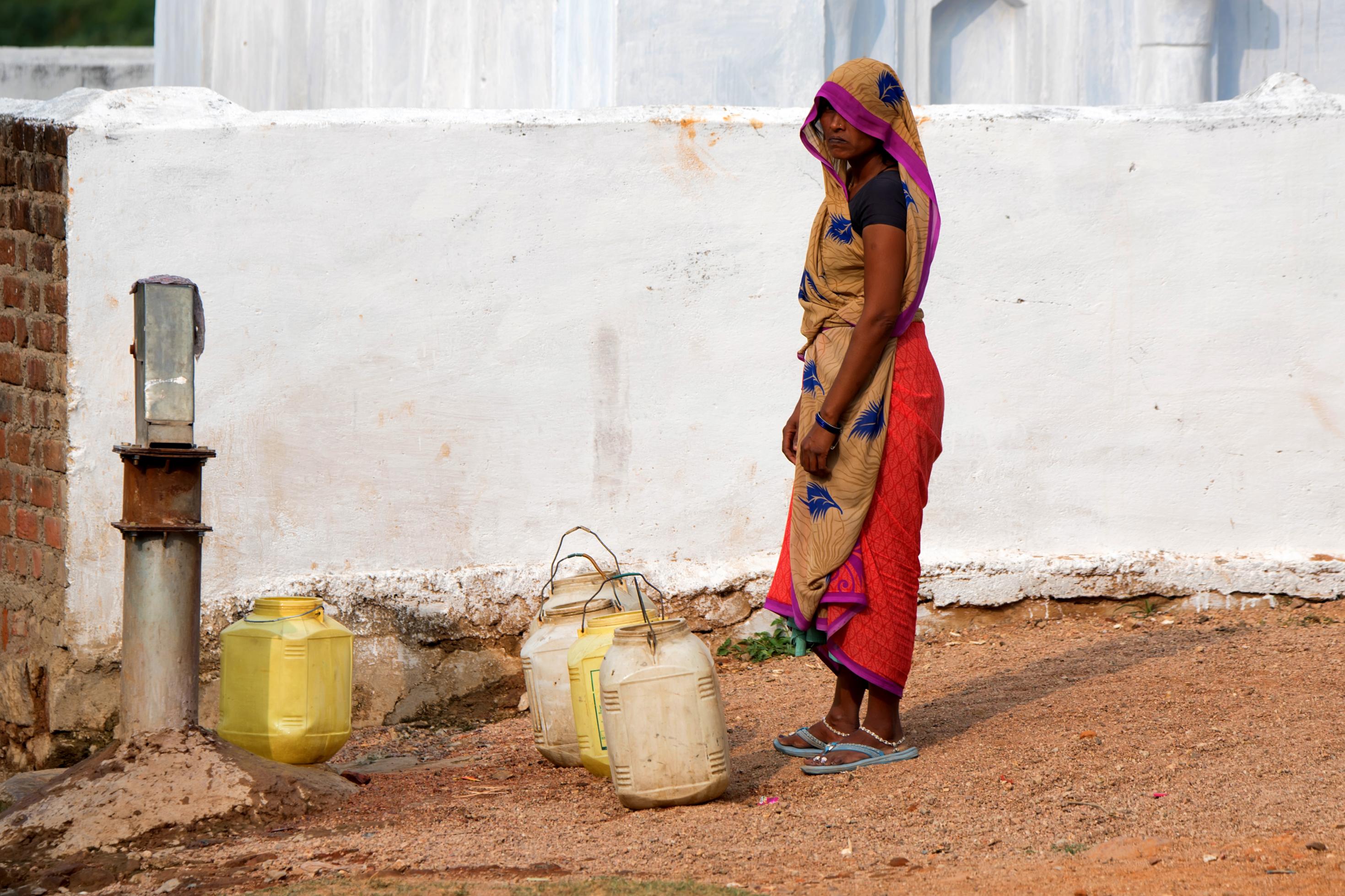Eine indische Frau steht vor einer Pumpe, um Wasser zu besorgen.