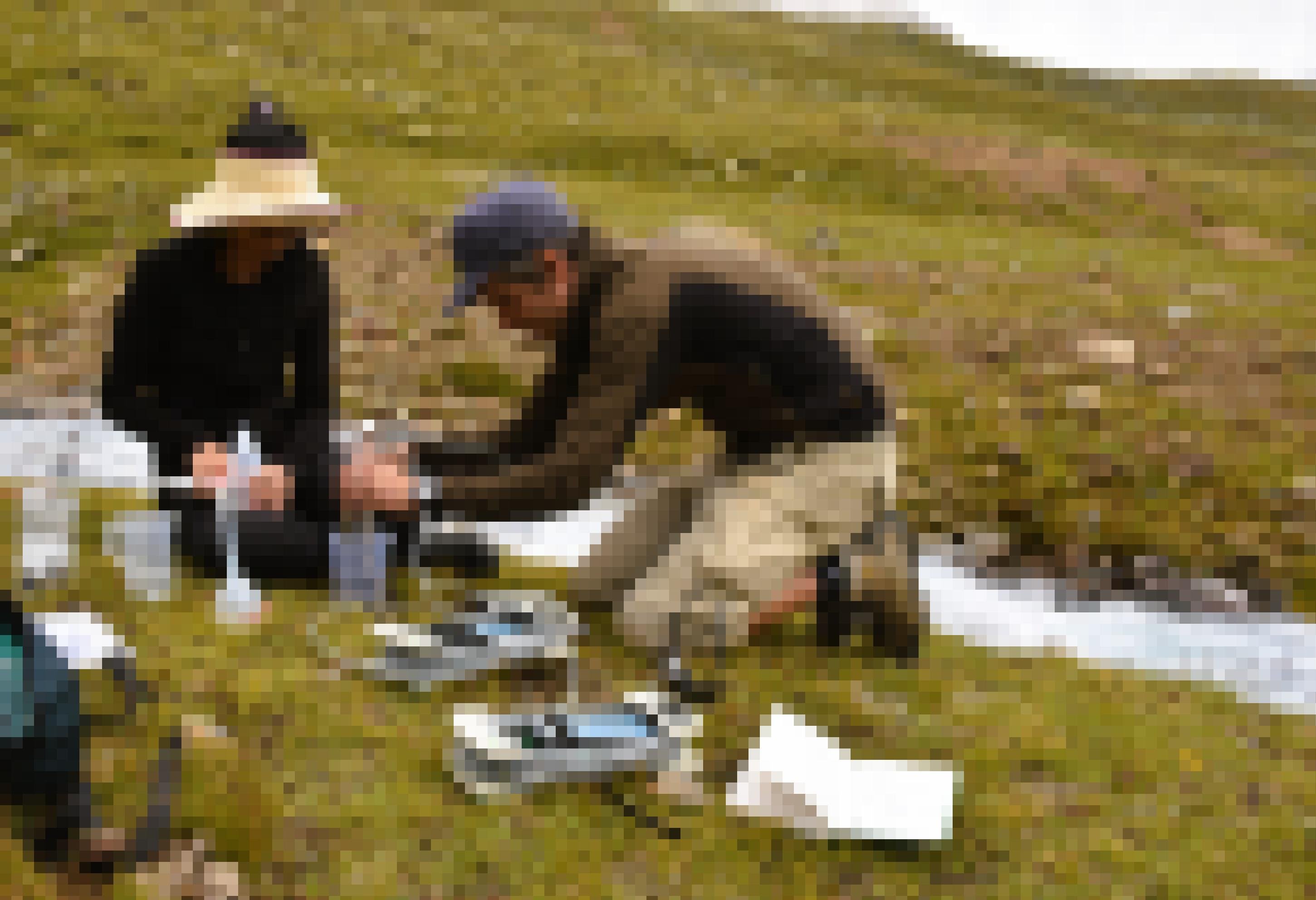 Ein Mann und eine Frau hantieren mit Laborgerät auf der Wiese neben einem Gebirgsbach