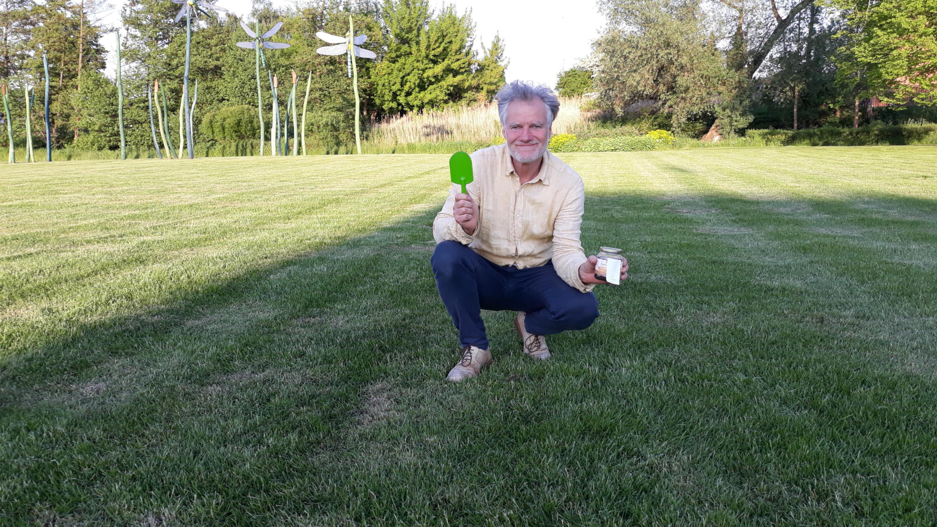 Ein Mann auf einer glatt gemähten Wiese, vermutlich ein Fußballfeld, mit kleiner Schaufel und Schraubglas