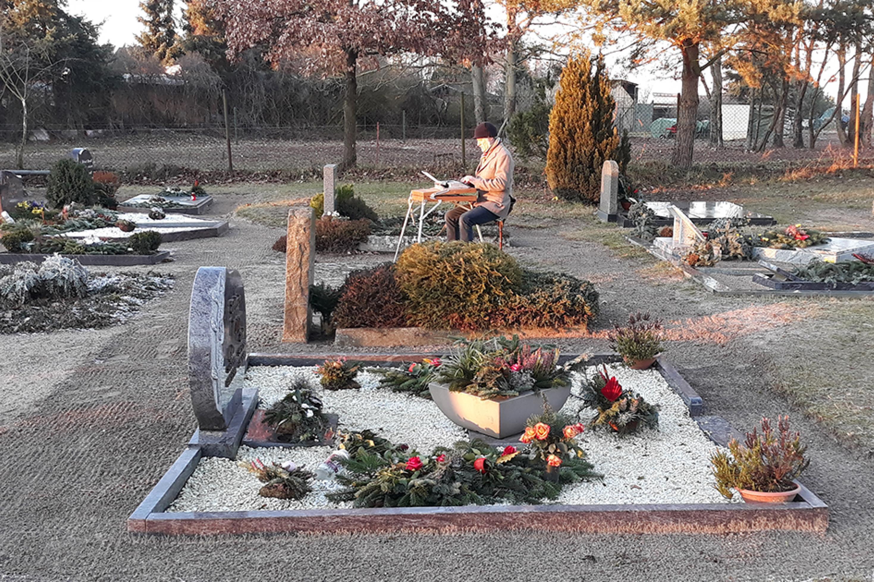 Fieldwriter Gerhard Richter sitzt mit seinem Klappschreibtisch auf einem Friedhof neben Gräbern