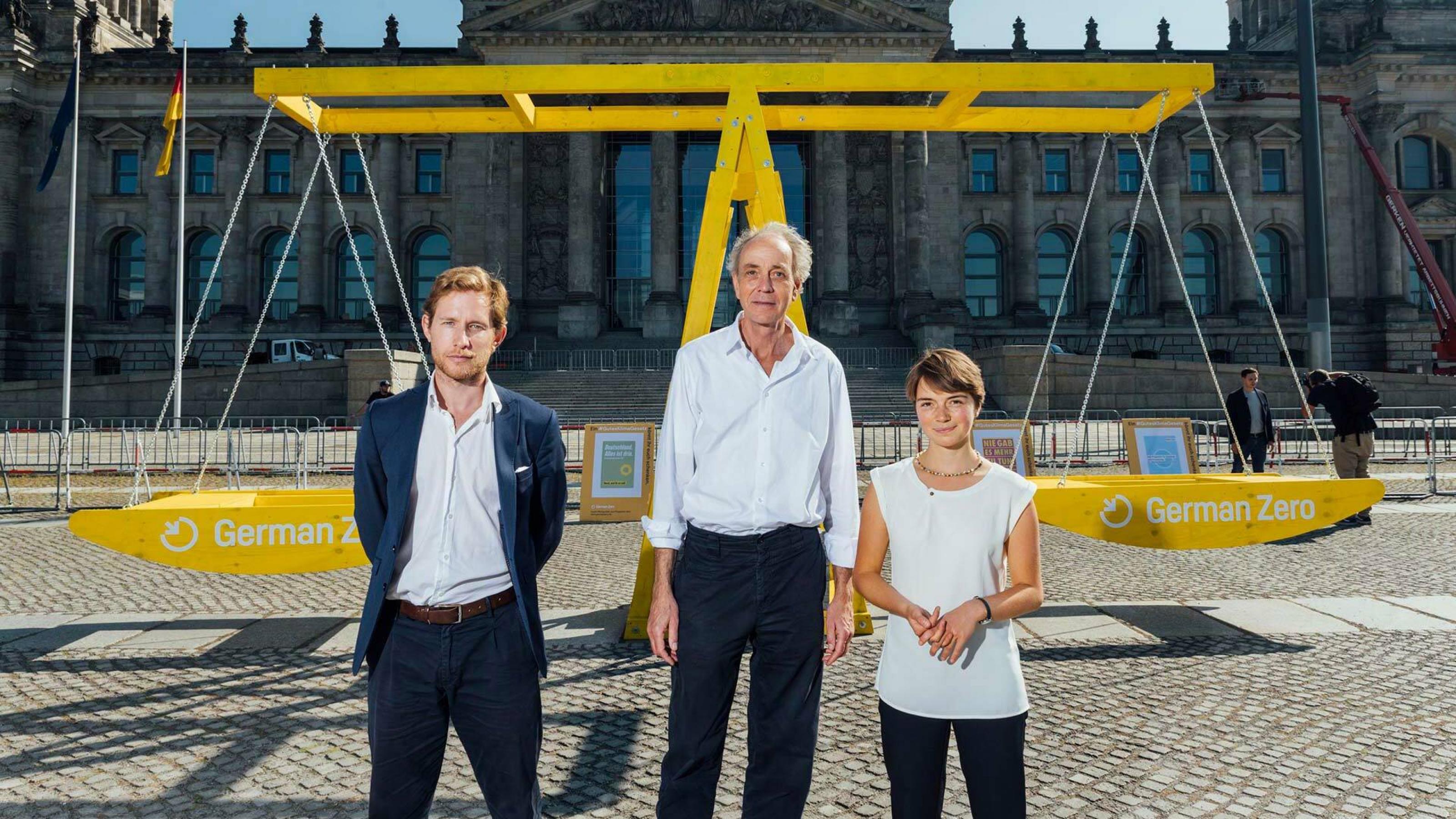Julian Zuber, Stephan Breidenbach und Lea Nesselhauf vor einer großen symbolischen Waage vor dem Reichstagsgebäude in Berlin