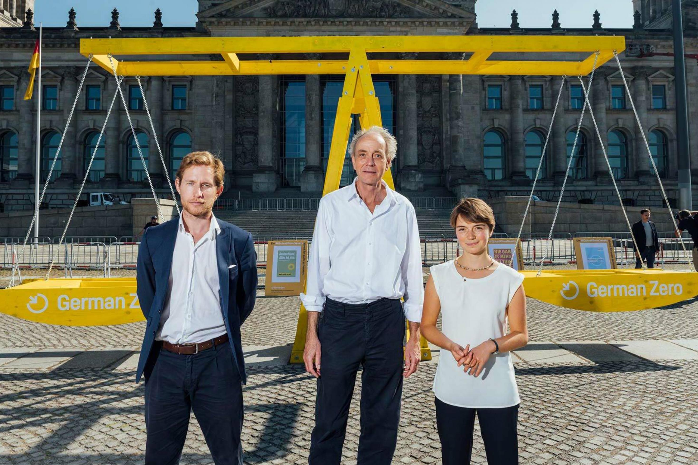 Julian Zuber, Stephan Breidenbach und Lea Nesselhauf vor einer großen symbolischen Waage vor dem Reichstagsgebäude in Berlin