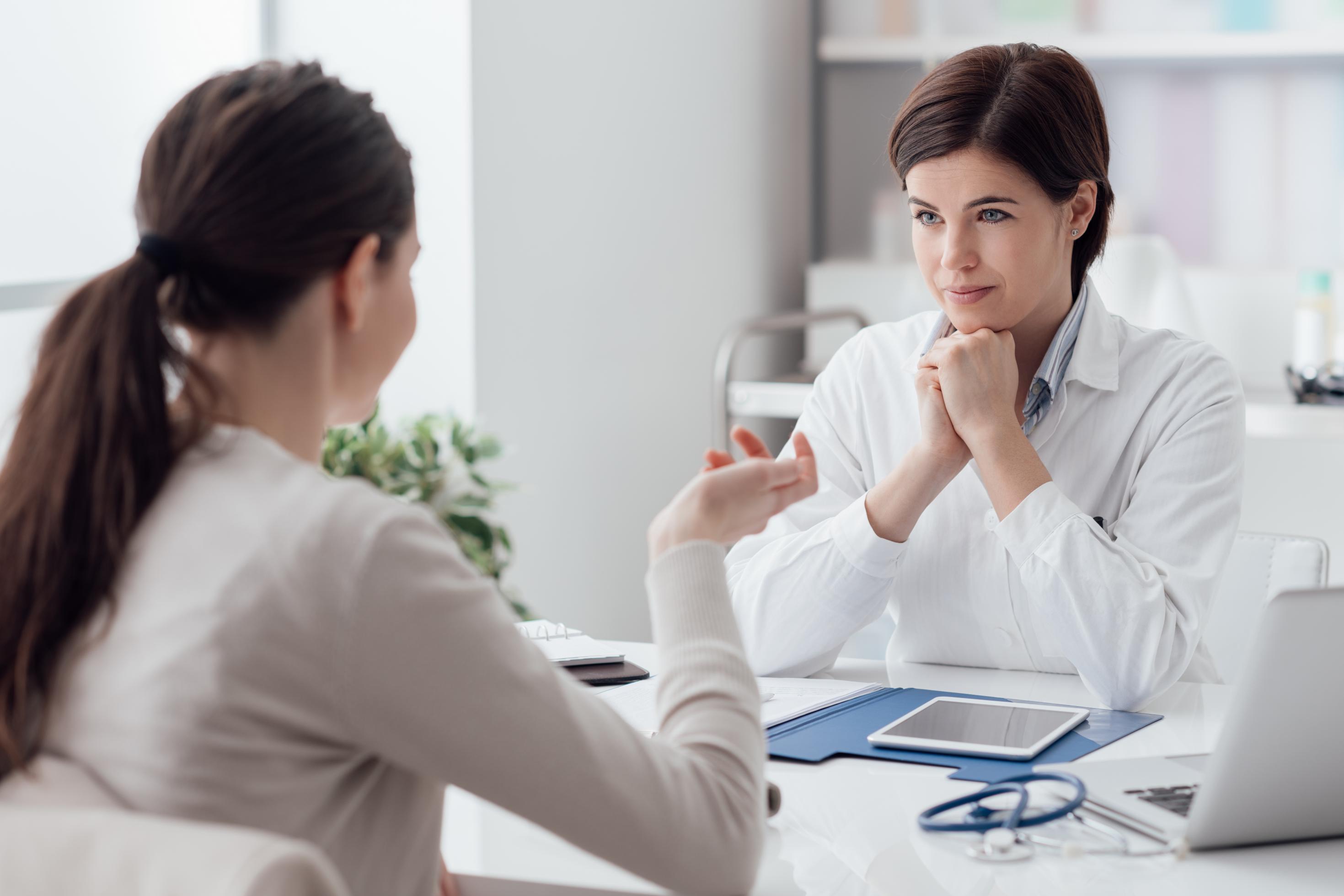 Eine Ärztin mit Stethoskop und Tablet hört einer Patientin zu.