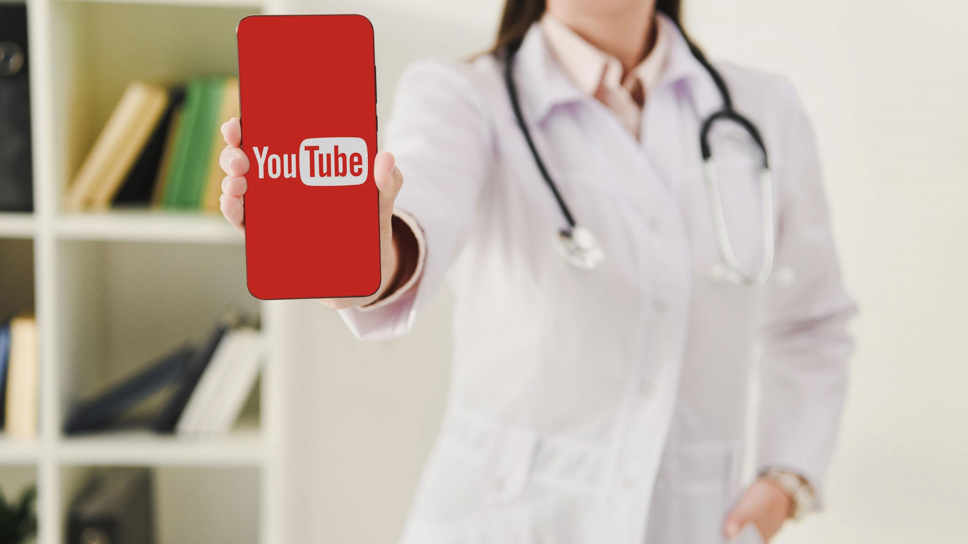 Eine Ärztin hält ein Smartphone mit dem YouTube-Logo.