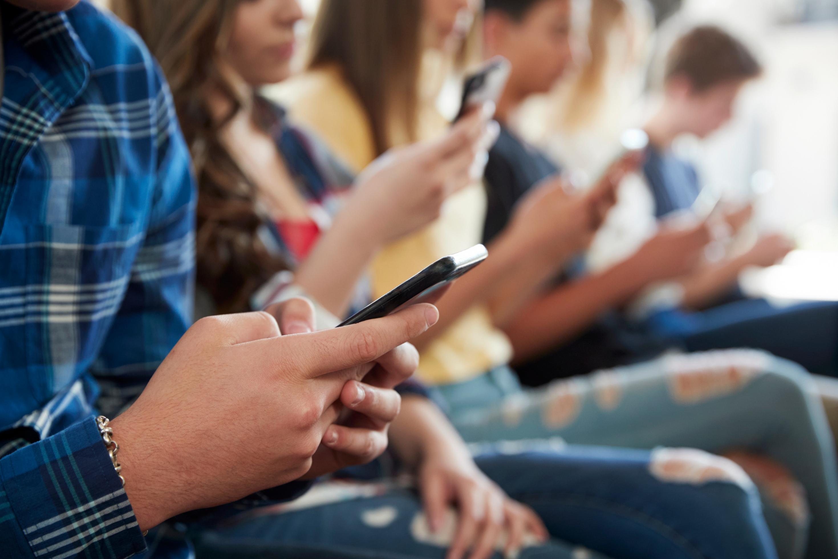 Jugendliche sitzen in einer Reihe und benutzen Smartphones.