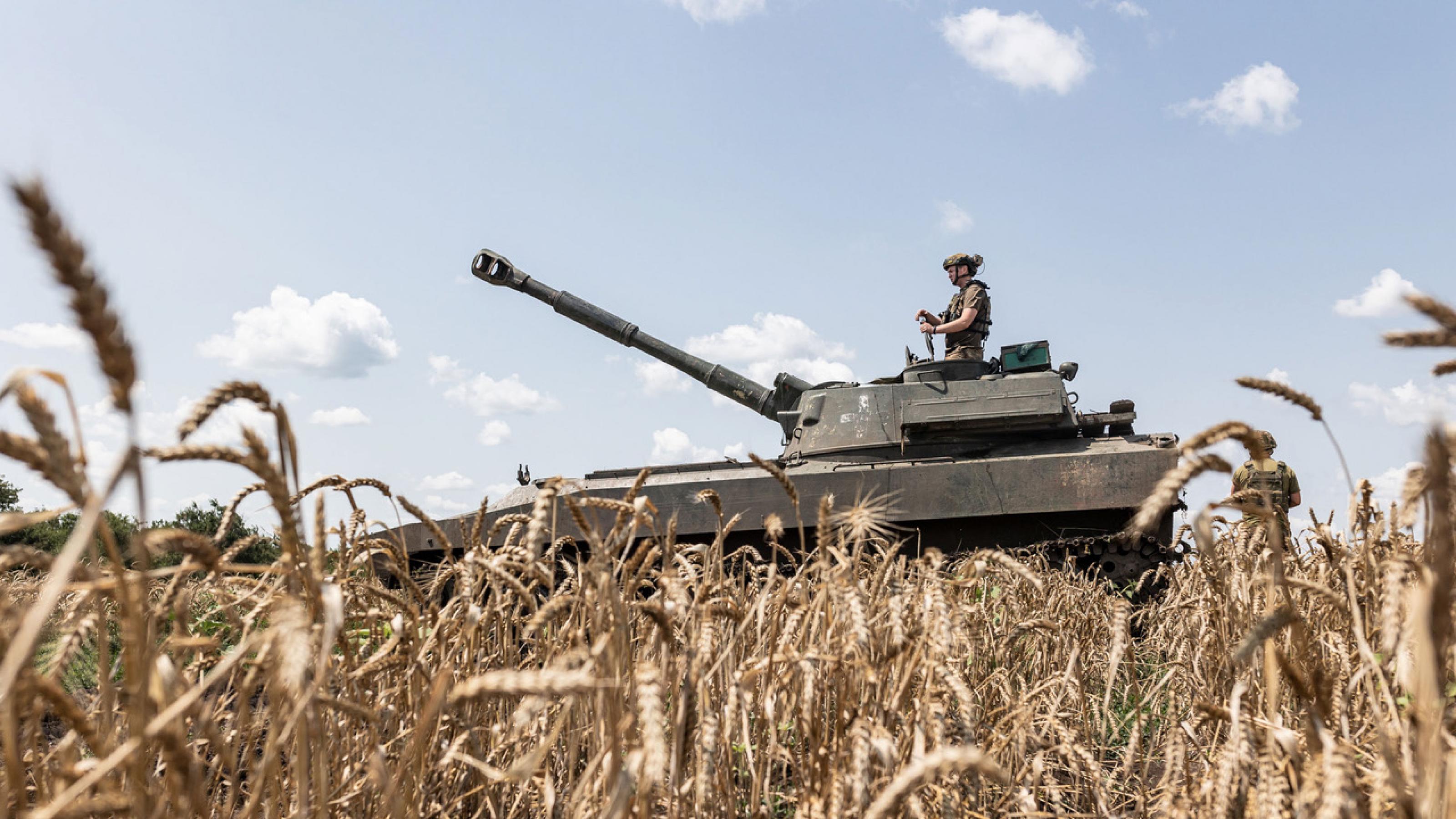 Eine Totale zeigt einen Panzer inmitten eines Getreidefeldes. Ein ukrainischer Soldat steht mit dem Panzer mitten im Getreidefeld. Der Soldat verteidigt das Gebiet Donezk gegen die russische Armee.