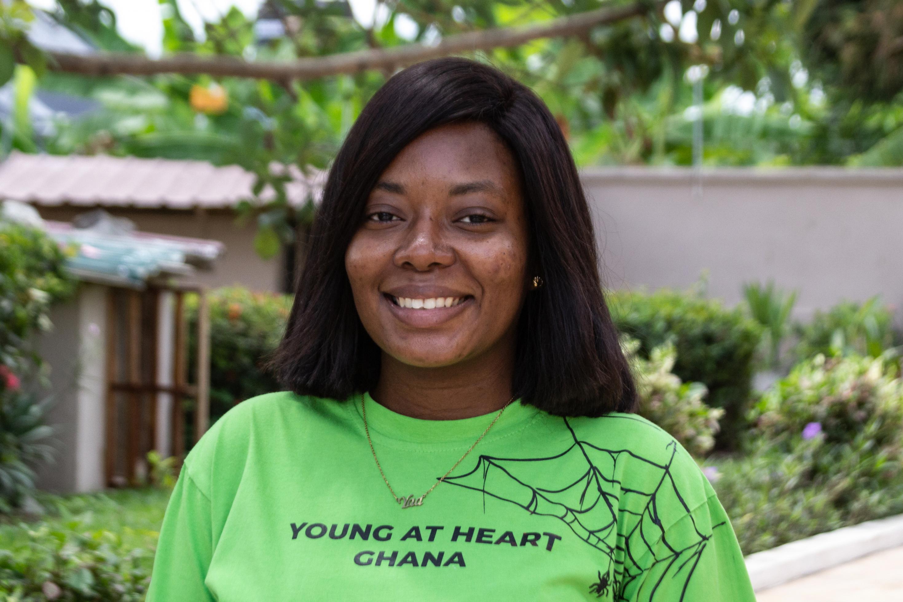 Das Portrait einer Frau, schwarze, glatte Haare. Sie lächelt, trägt ein leuchtend grünes T-Shirt mit der Aufschrift Young At Heart.