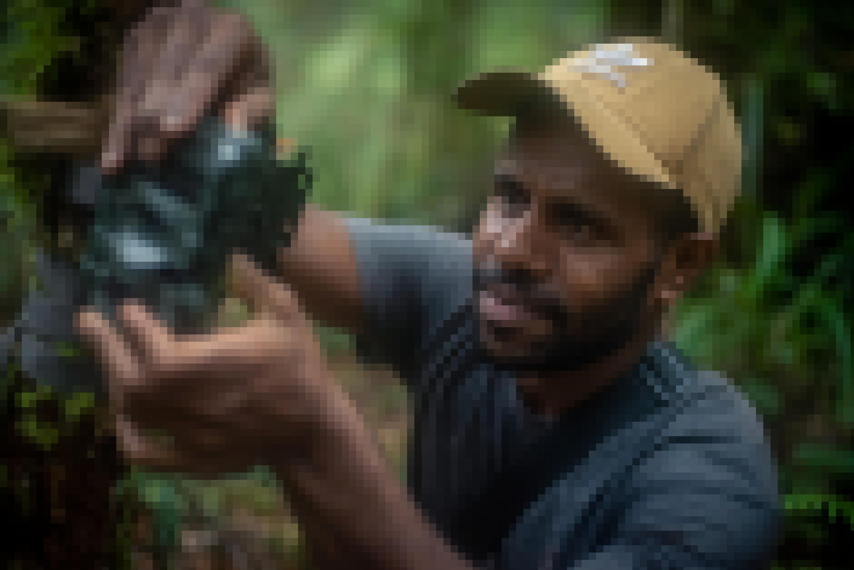 Ein Mann mit dunkler Haut hantiert im Regenwald mit einer Kamerafalle.