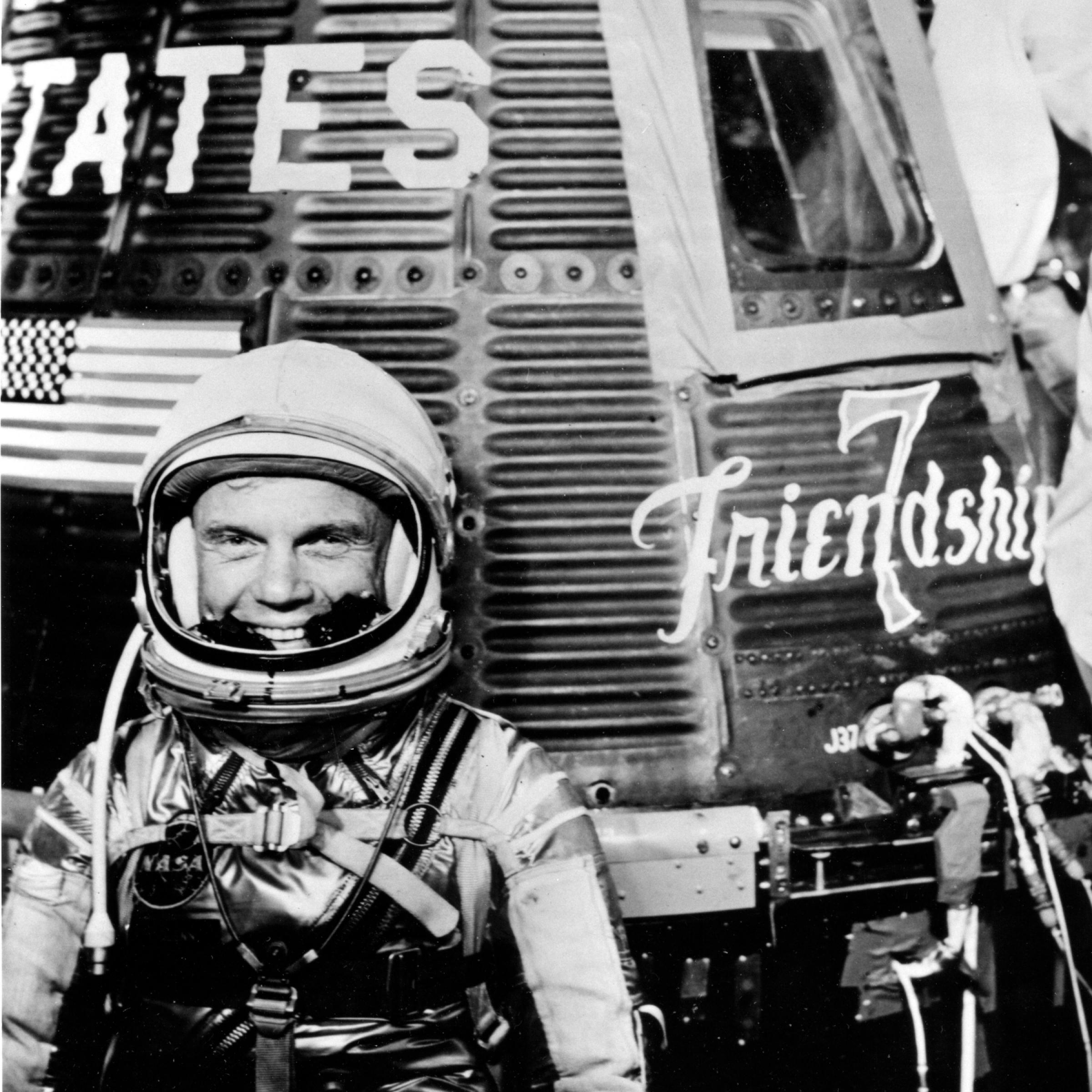 Ein Astronaut, John Glenn, im Raumanzug steht vor einer Mercury-Raumkapsel.