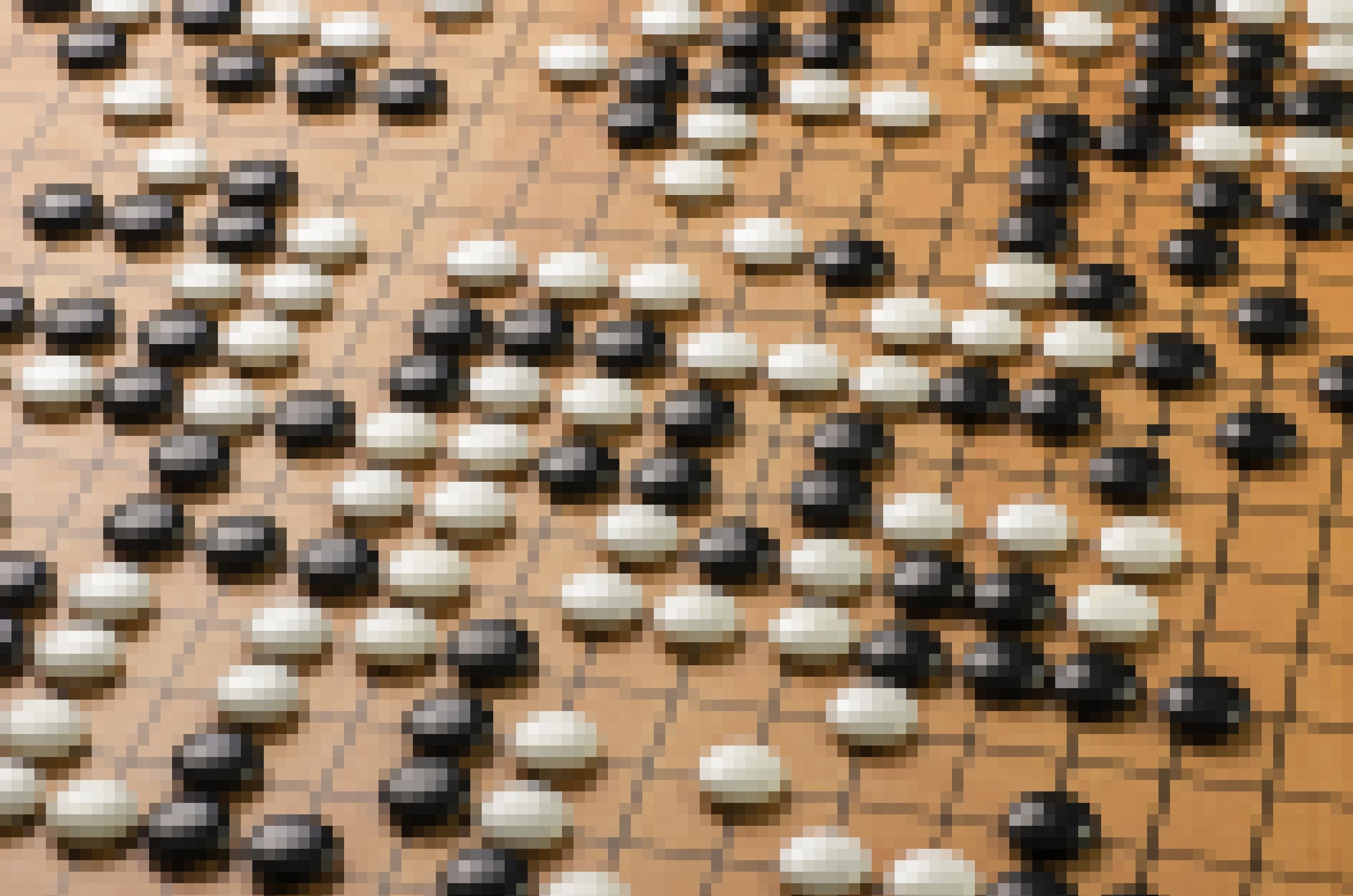 Zahlreiche schwarze und weiße linsenförmige Spielsteine liegen auf einem braunen Spielbrett. Das Brett ist von vielen schwarzen senkrecht wie waagerecht verlaufenden Linien in kleine Quadrate geteilt. Die Spielsteine liegen auf den Schnittpunkten jeweils zweier Linien.
