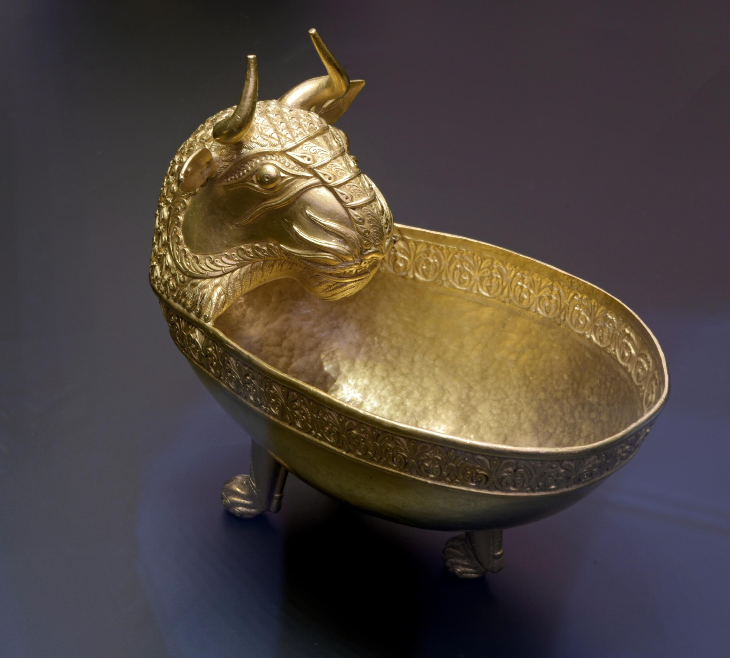 Das Bild zeigt eine goldene Schale, die auf drei Füßen aufgestellt wird. Sie geht in den Kopf eines gehörnten Löwen über und ist sehr fein gearbeitet.