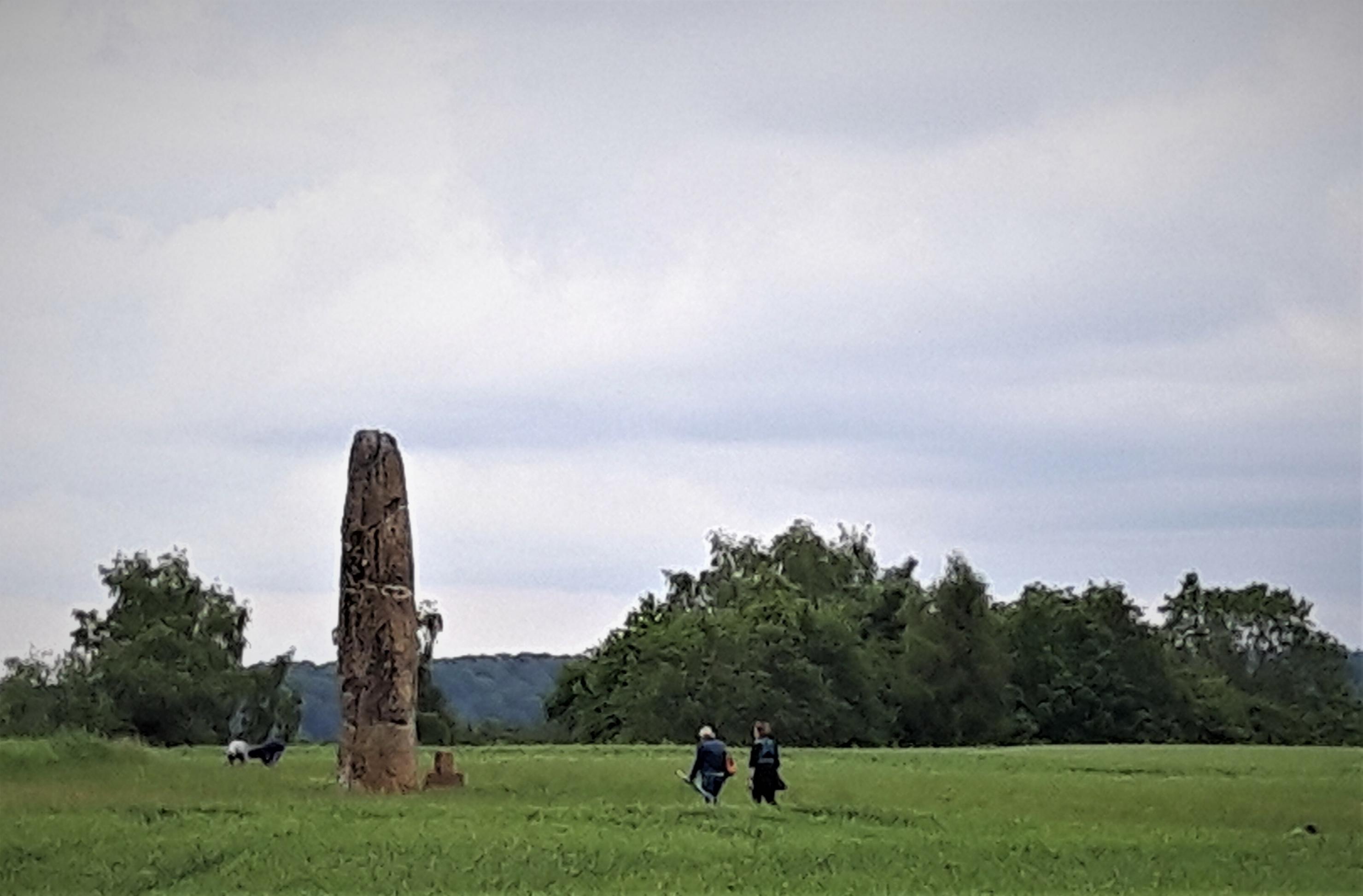 Inmitten einer üppigen Wiese überragt eine Art Hinkelstein die Spaziergänger um das etwa Vierfache.