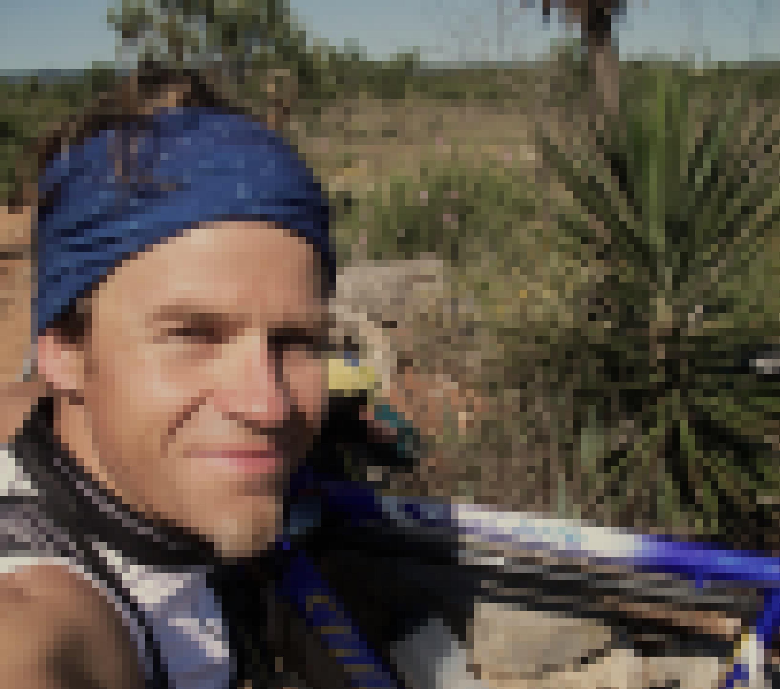 Selfie des Reporters zusammen mit seinem Rennrad, am Rande eines rotbraunen Weges, den mediterrane Pflanzen säumen.